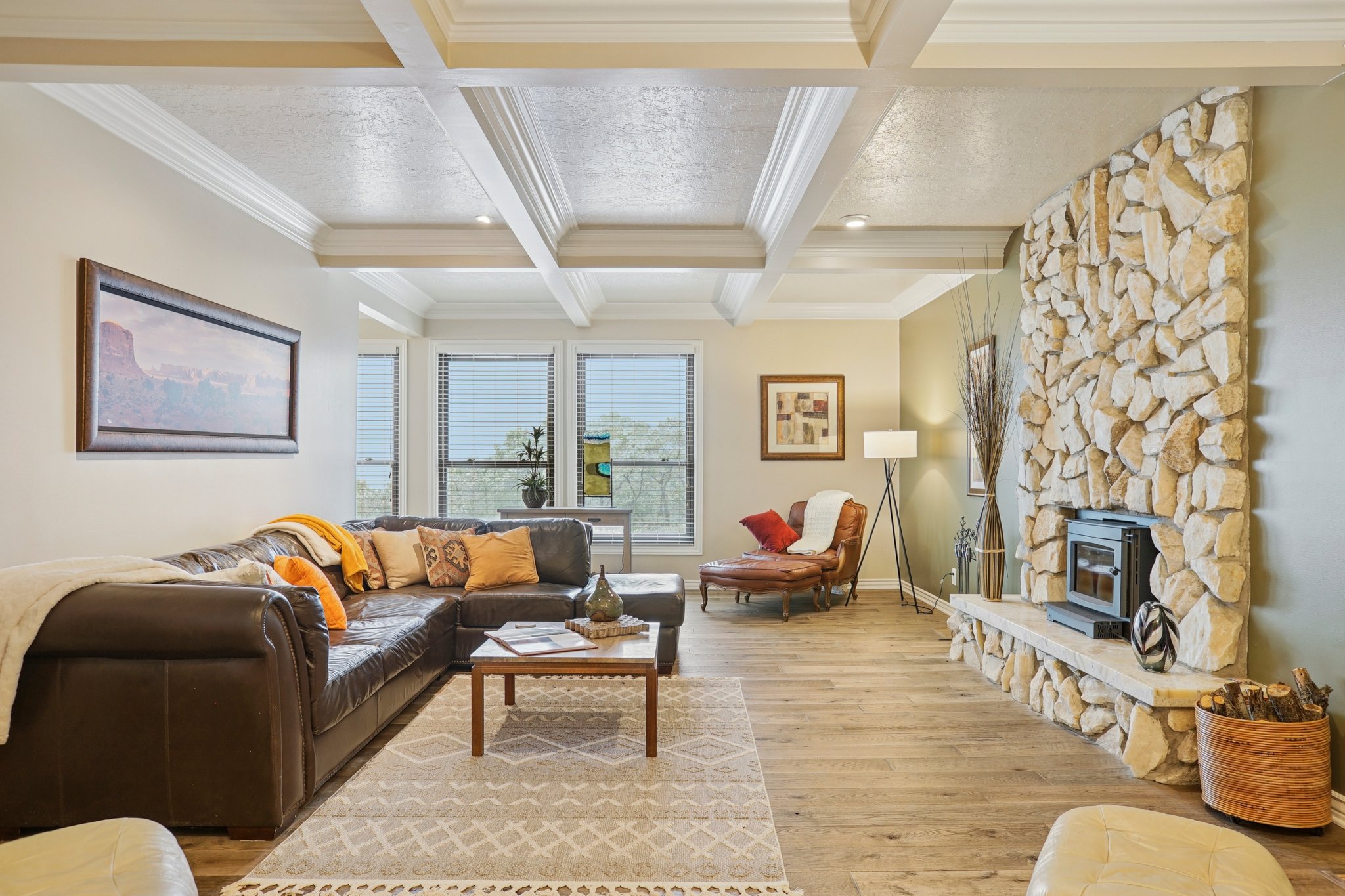 Living area featuring a stone-clad fireplace with hearth, wood-finish flooring, coffered ceiling, and multiple windows