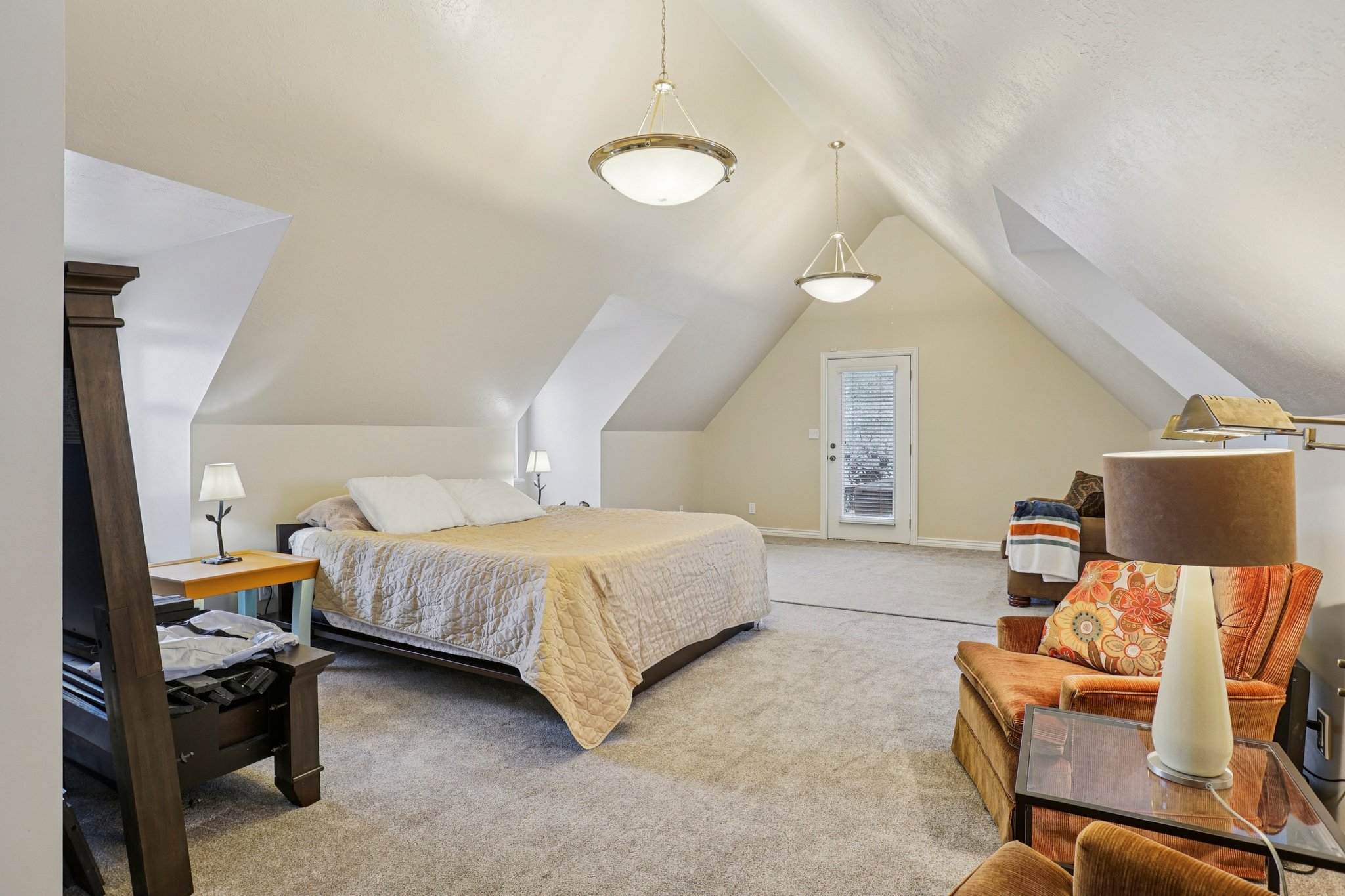 Spacious attic room featuring sloped ceilings, recessed wall sections, and light-colored carpeting