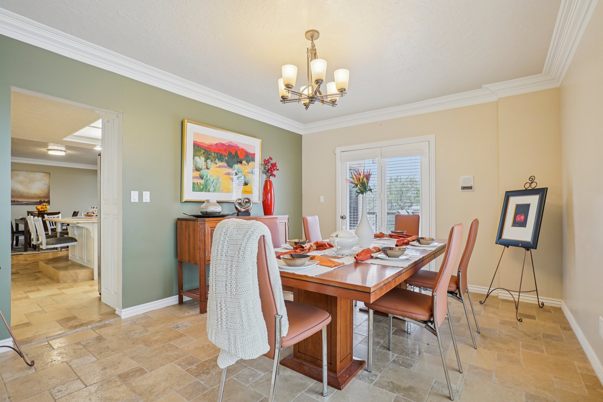 Formal dining area featuring tile flooring, crown molding, a built-in chandelier, and a large window with plantation shutters