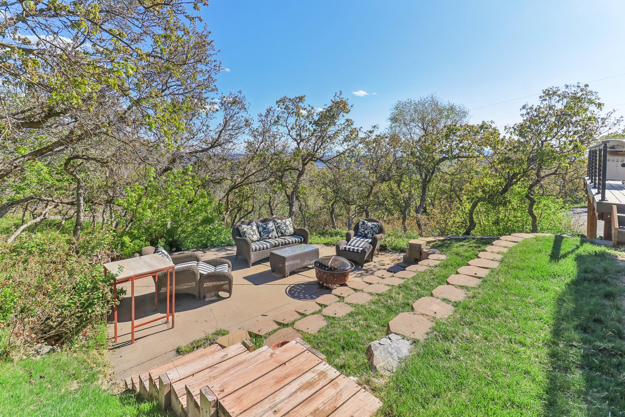 Outdoor patio with a stone paver path, surrounded by mature trees and natural landscaping