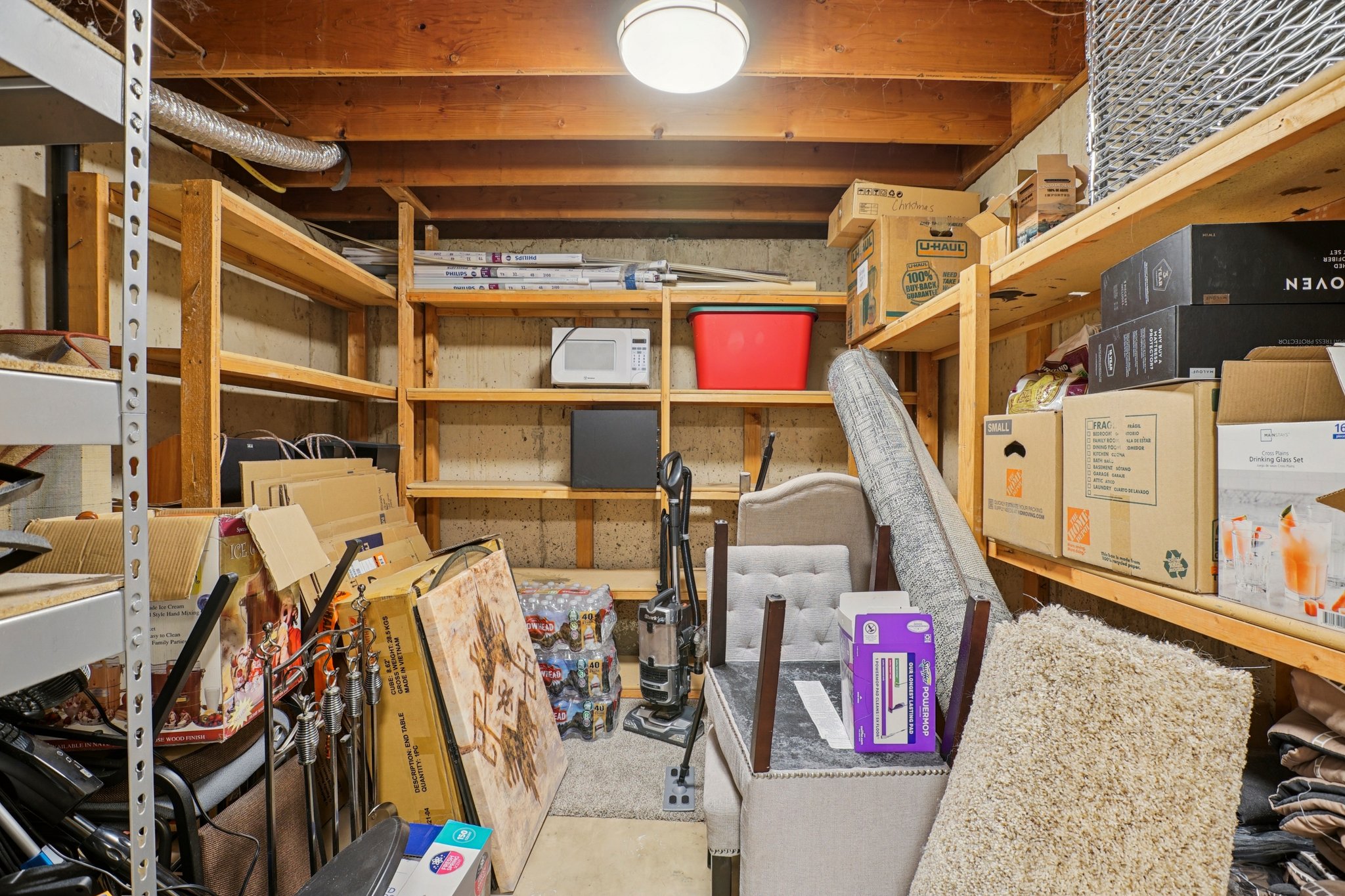 Basement storage area featuring extensive wooden shelving, exposed ceiling joists, and a ceiling-mounted light fixture
