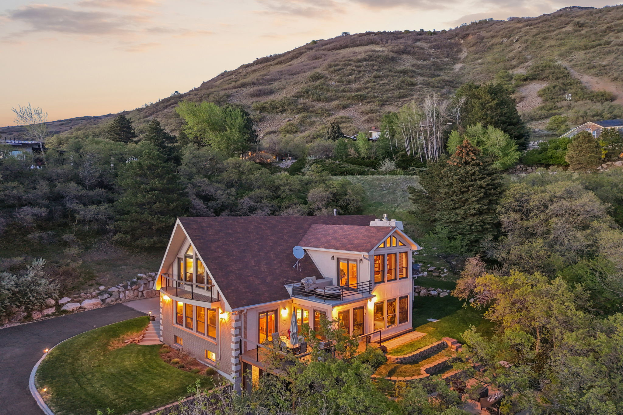 Alpine-style home featuring multiple balconies, a terraced landscape, a paved driveway, and extensive natural surroundings
