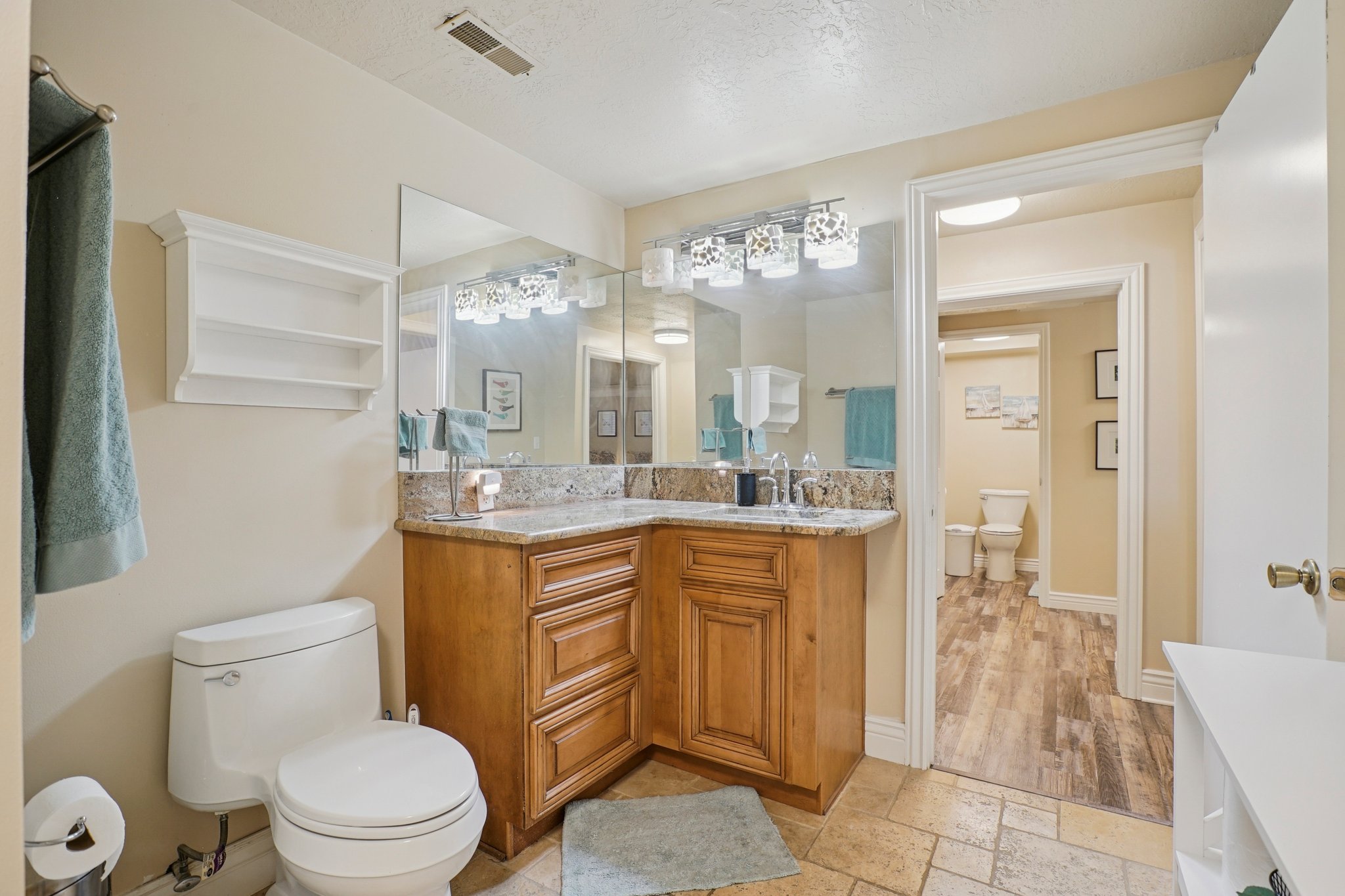 Bathroom featuring a corner vanity with a granite countertop, dual sinks, and light wood-finish cabinetry