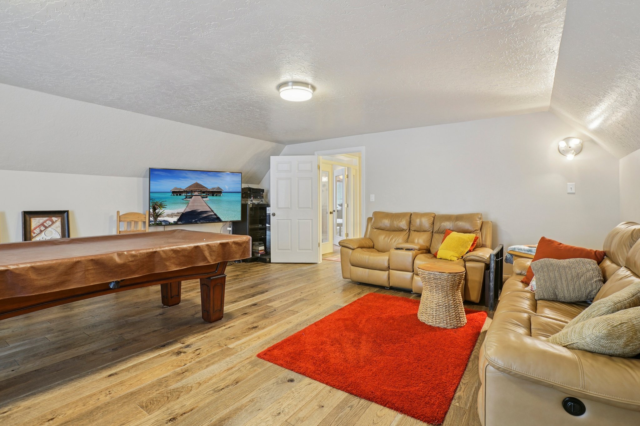 Spacious room featuring wood-finish flooring, light-toned walls, and a sloped ceiling