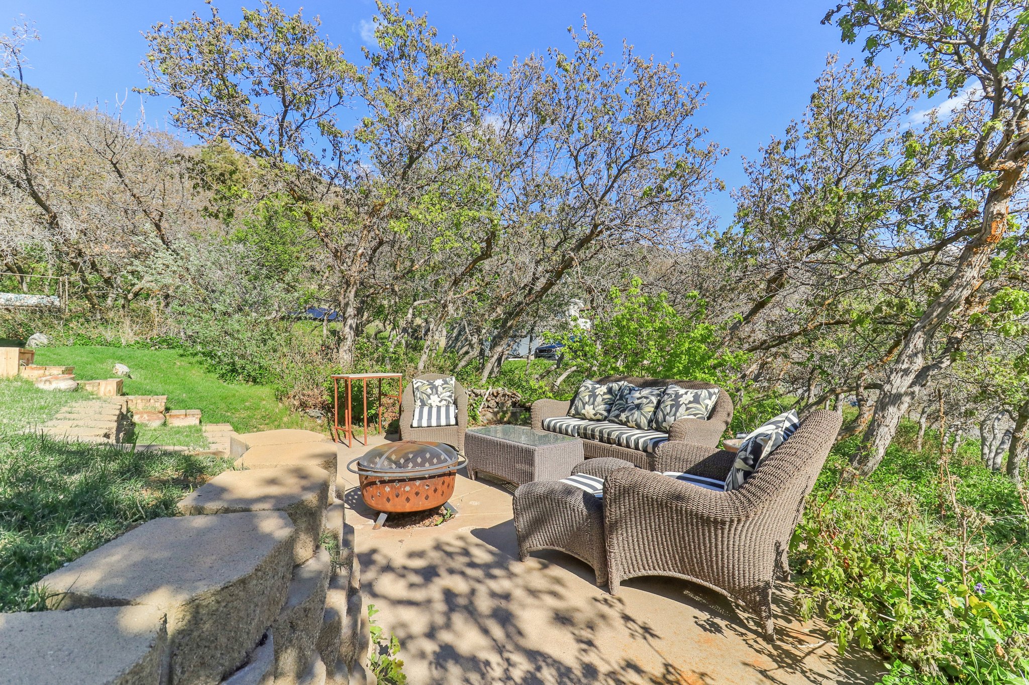 Stone patio with a built-in fire pit, surrounded by lush natural landscaping and mature trees