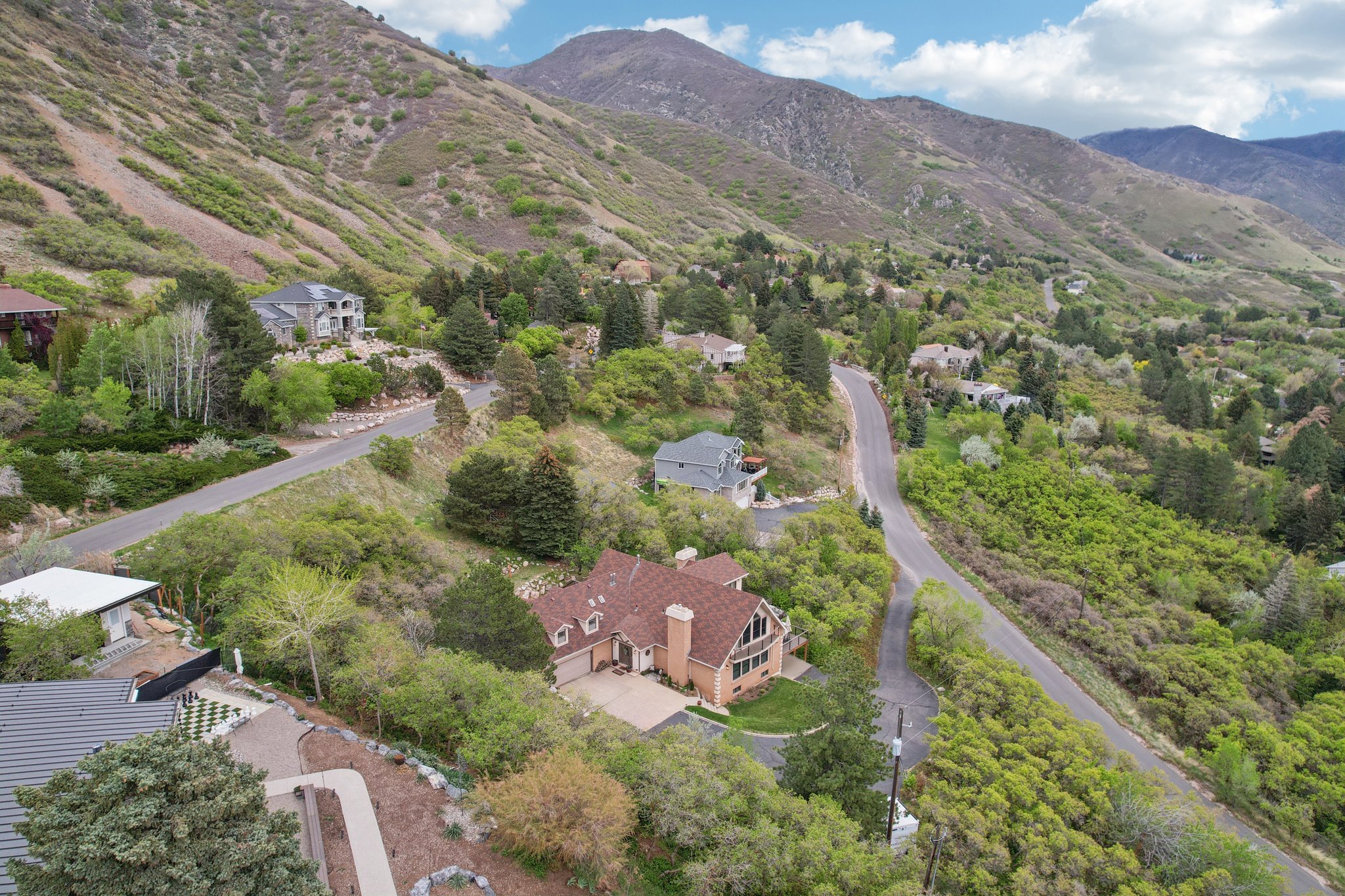 Sloping mountain terrain surrounds a residential property with a multi-gabled roof and a prominent chimney