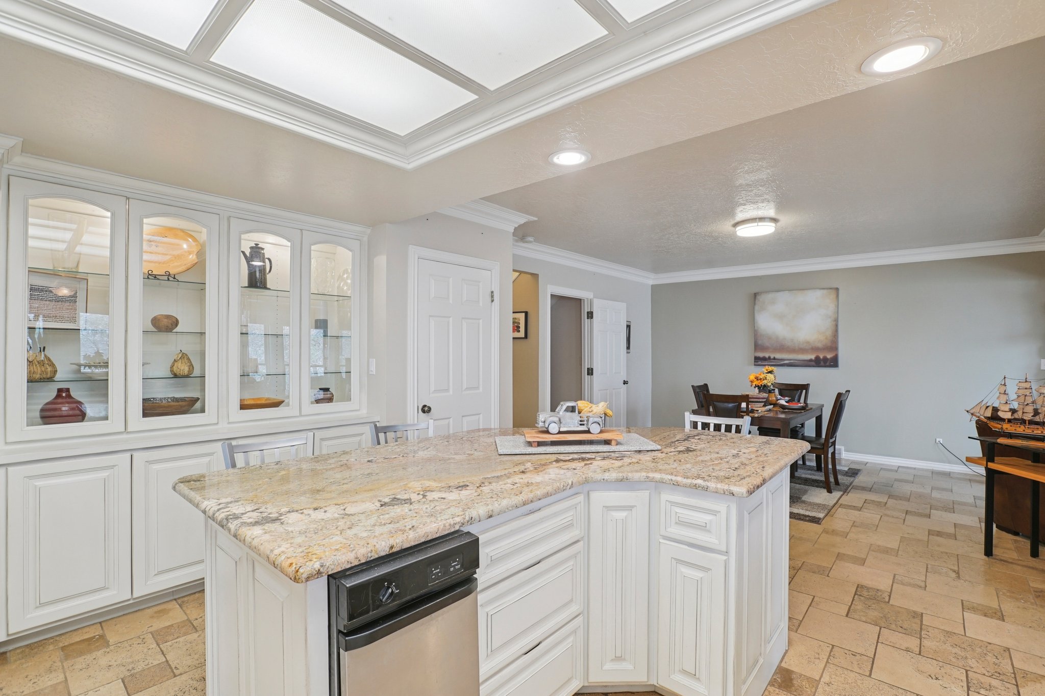 Kitchen area featuring a built-in display cabinet with glass fronts, recessed lighting, and a multi-toned stone countertop on the island