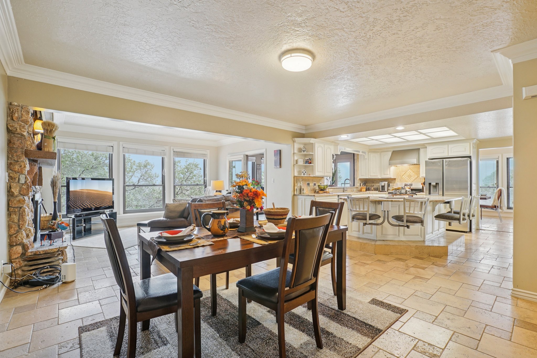Spacious open-concept living area featuring stone-finish flooring, a stone fireplace, and extensive window-line