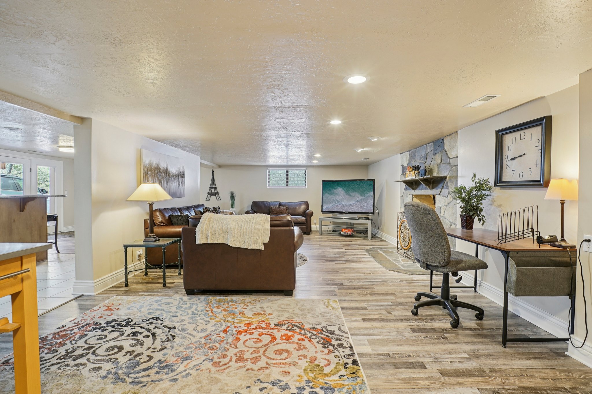 Open-concept living area featuring wood-finish flooring, recessed lighting, and a stone-clad wall with a built-in mantel