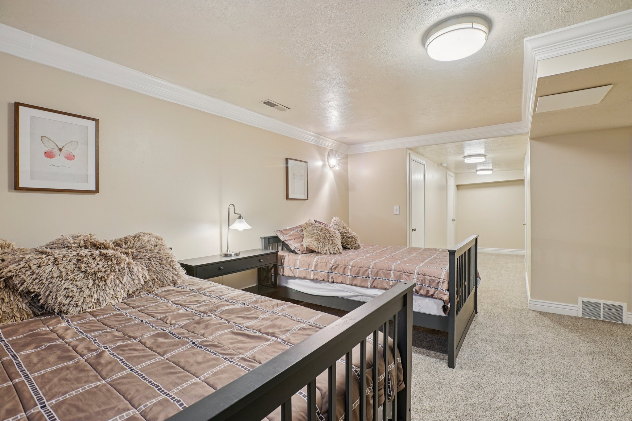 Carpeted room featuring two beds with black frames, crown molding, a built-in wall sconce, and a hallway with recessed lighting