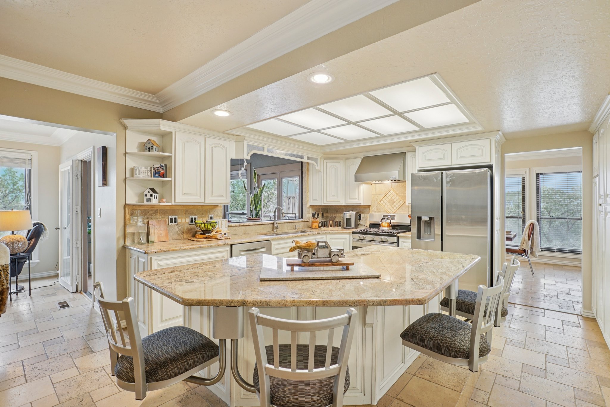 Kitchen featuring an angular island with seating, integrated stainless steel appliances, stone-finish countertops, white cabinetry, and a coffered ceiling with inset lighting