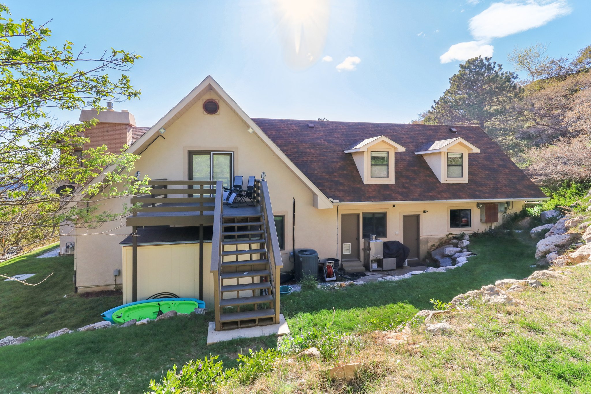 Two-story rear exterior featuring a deck with stairs, two dormer windows, and a lower-level patio