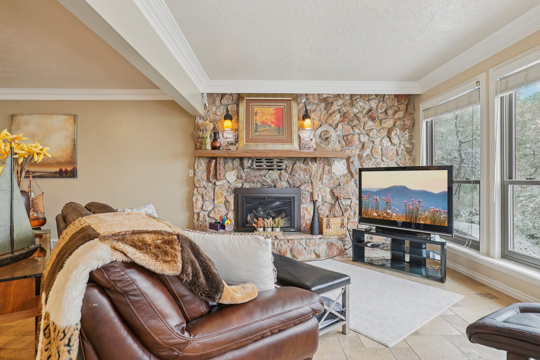 Living area featuring a stone fireplace with a wood mantel, multiple windows providing exterior views, and tile flooring