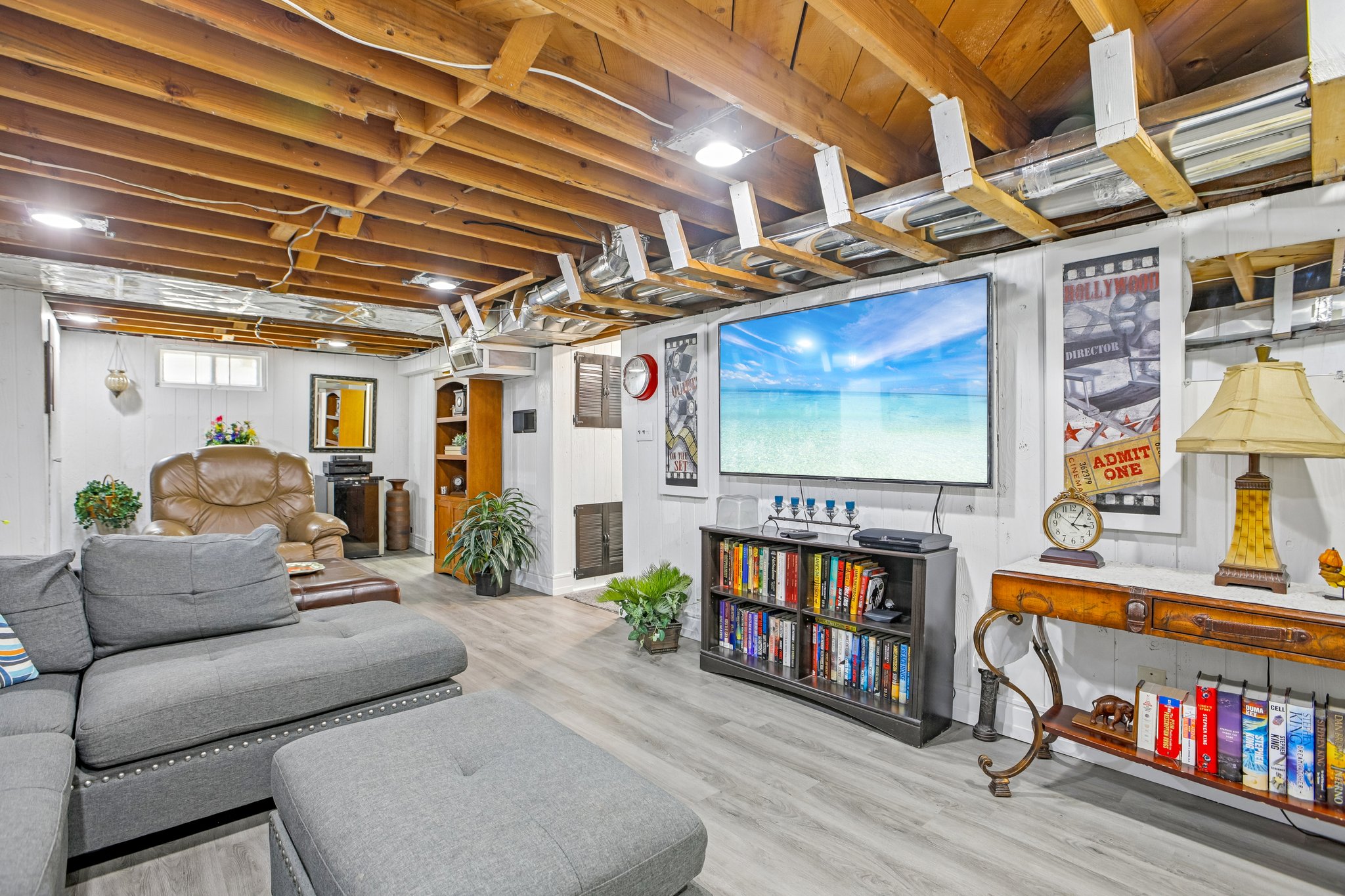 Lower level living area featuring a large media wall, exposed wood beam ceiling, recessed lighting, white paneling, and wood-finish flooring