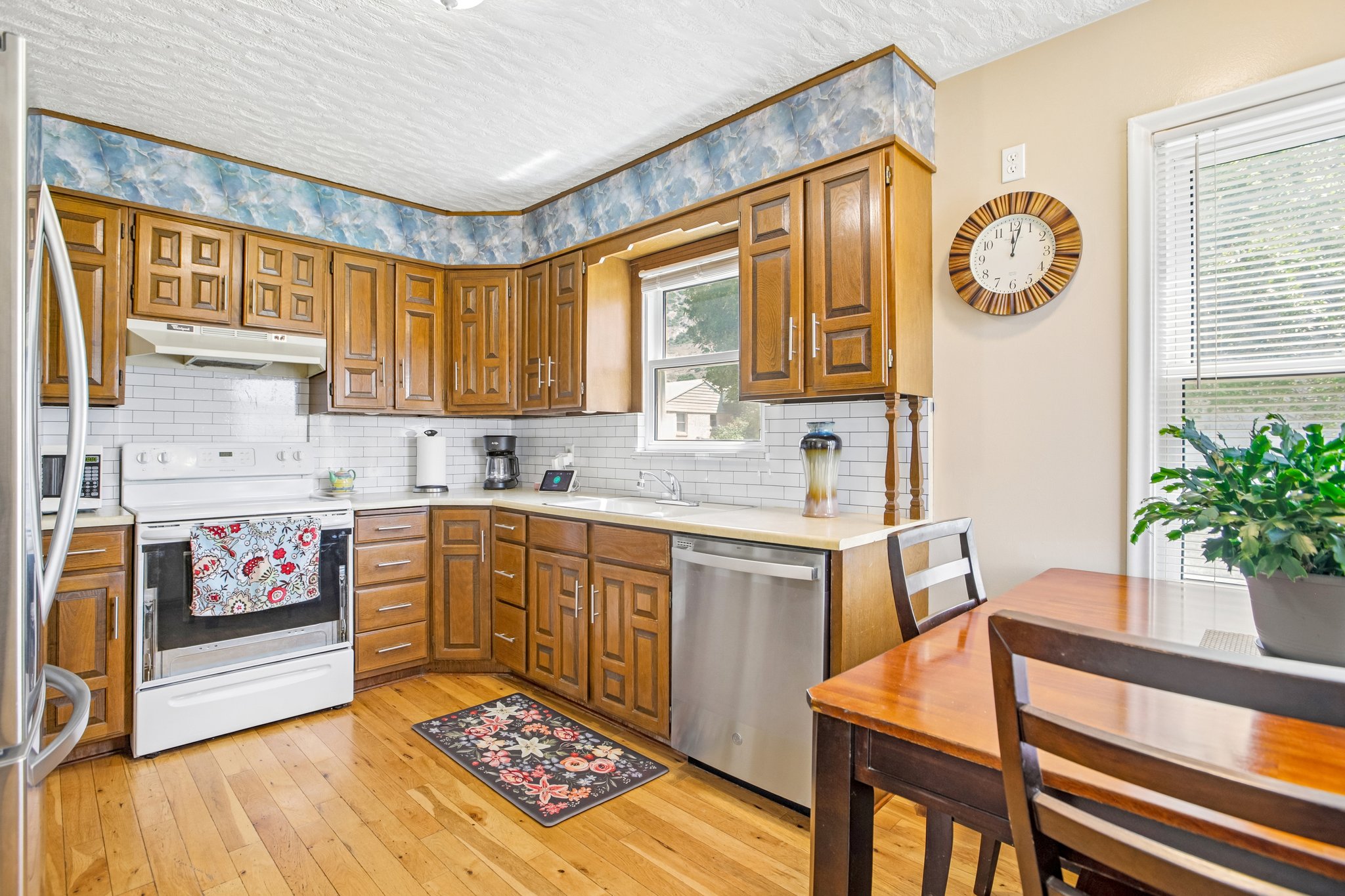 Kitchen featuring wood-finish flooring, wood cabinetry, white subway tile backsplash, light-toned countertops, and a stainless steel dishwasher
