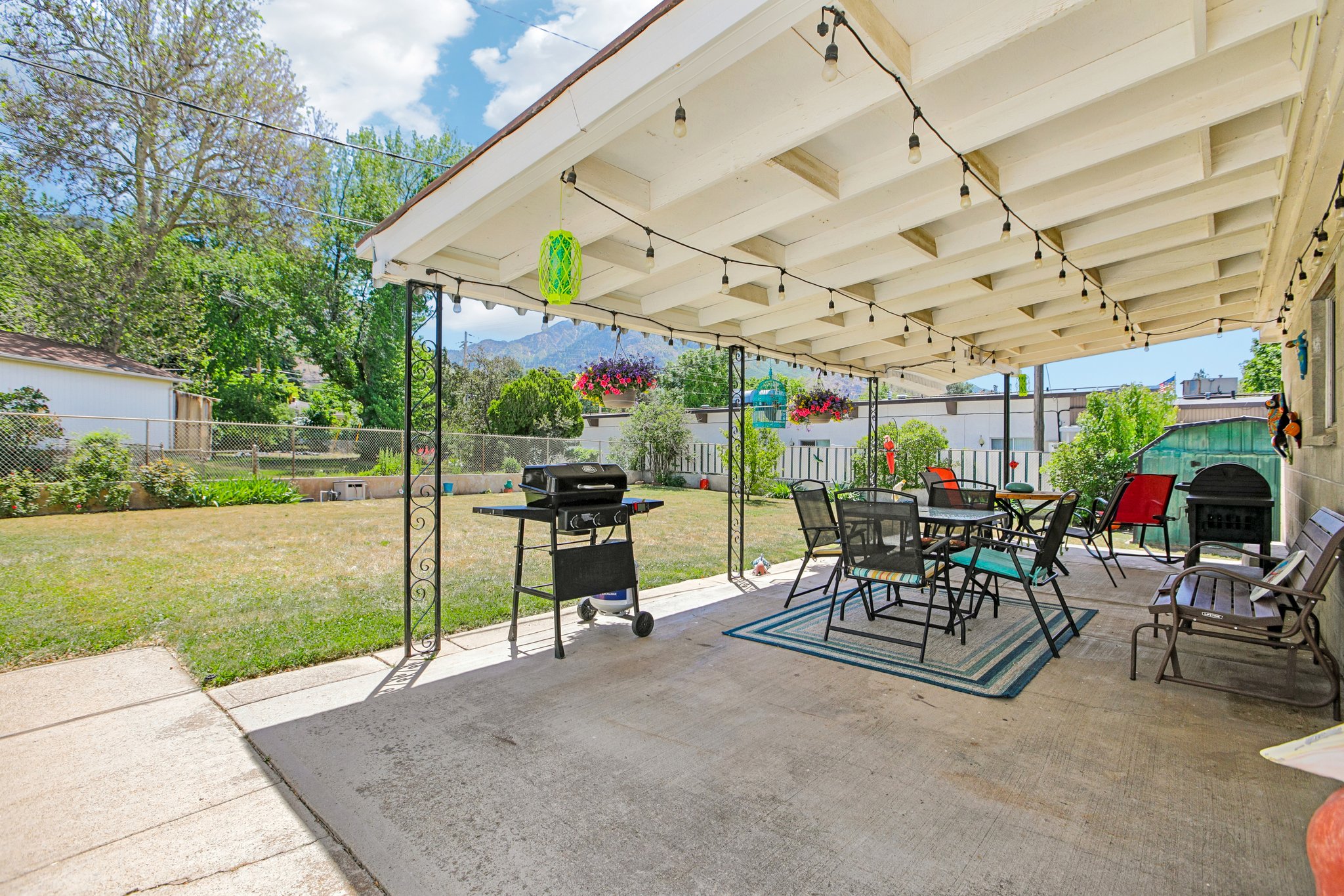 Covered concrete patio featuring decorative metal supports, string lighting, and direct access to a spacious lawn