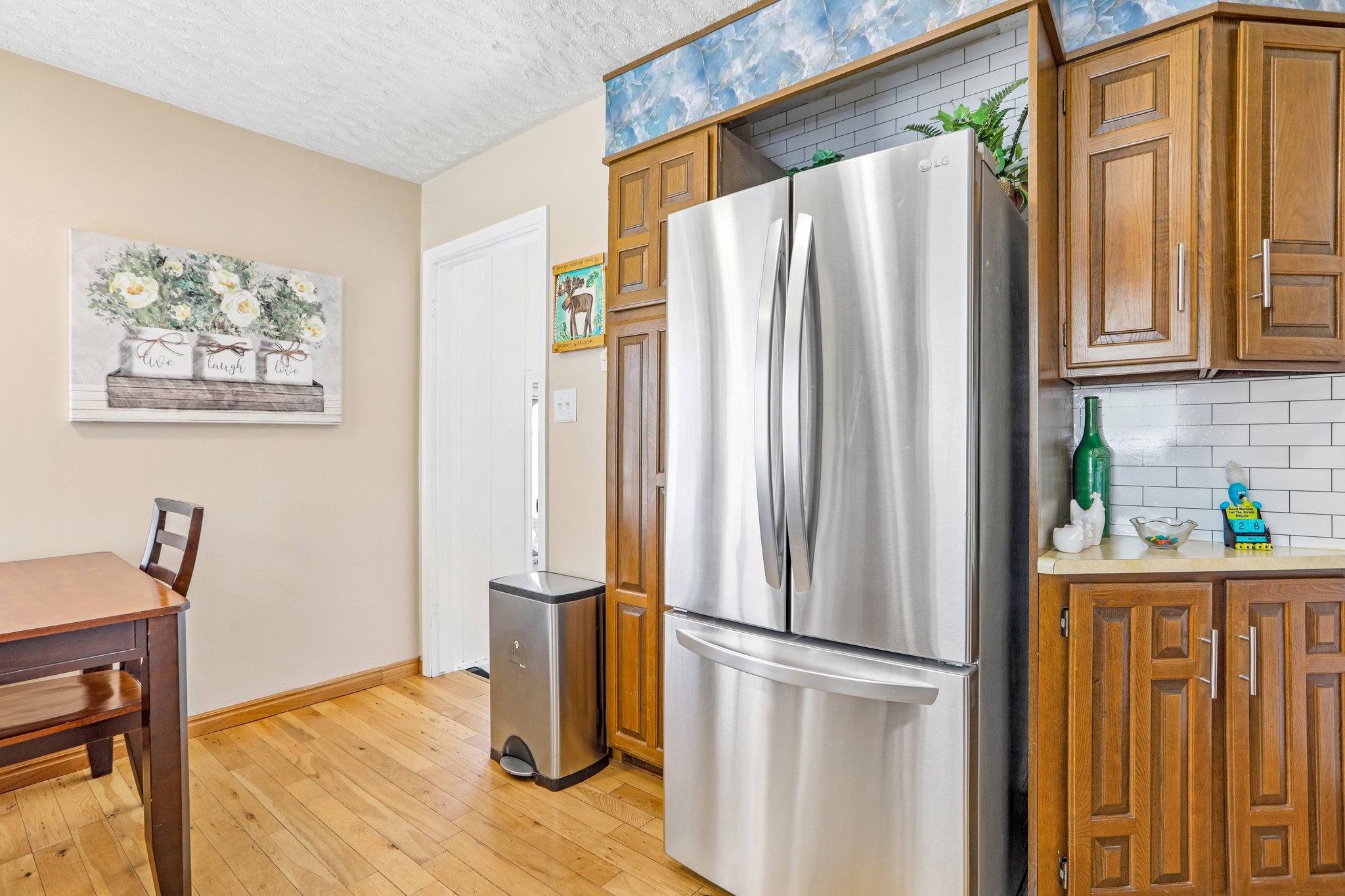 Kitchen area featuring a stainless steel French door refrigerator, wood-finish flooring, white subway tile backsplash, and wood cabinetry with metal hardware