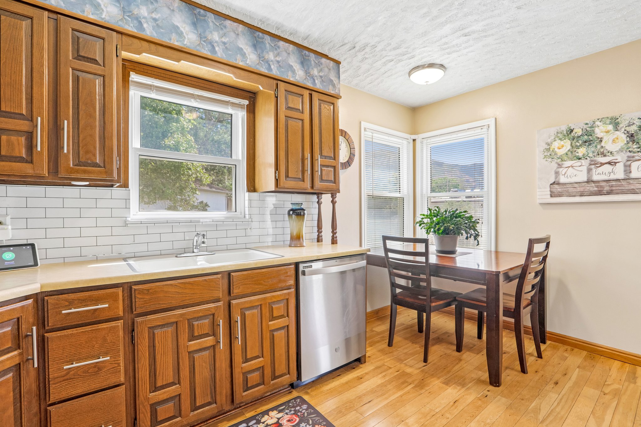 Kitchen featuring wood-finish cabinetry, light-toned countertops, subway tile backsplash, and a stainless steel dishwasher