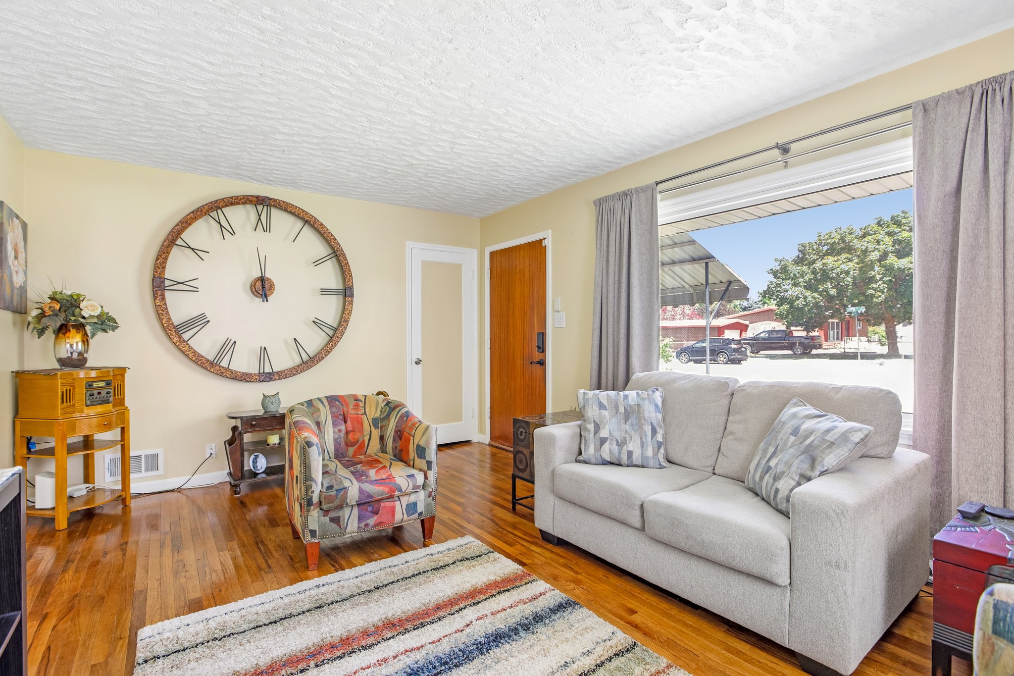 Spacious interior featuring hardwood flooring, light-colored wall paint, and a large window with privacy drapes