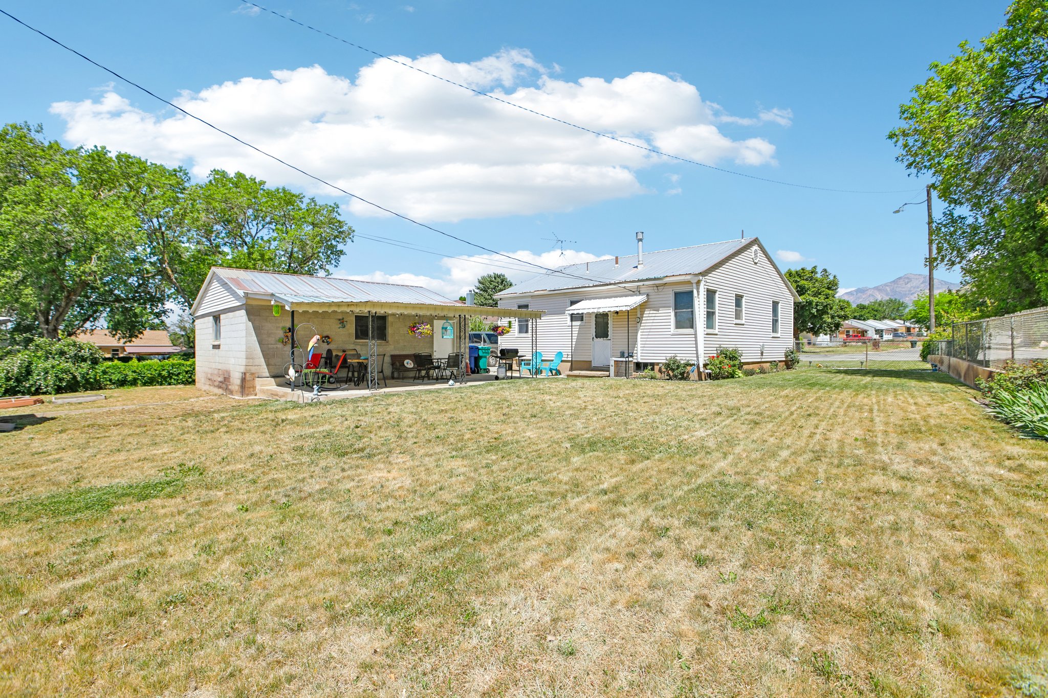 Expansive yard space featuring a detached building with a covered patio, a main residence with a side door, and distant mountain scenery
