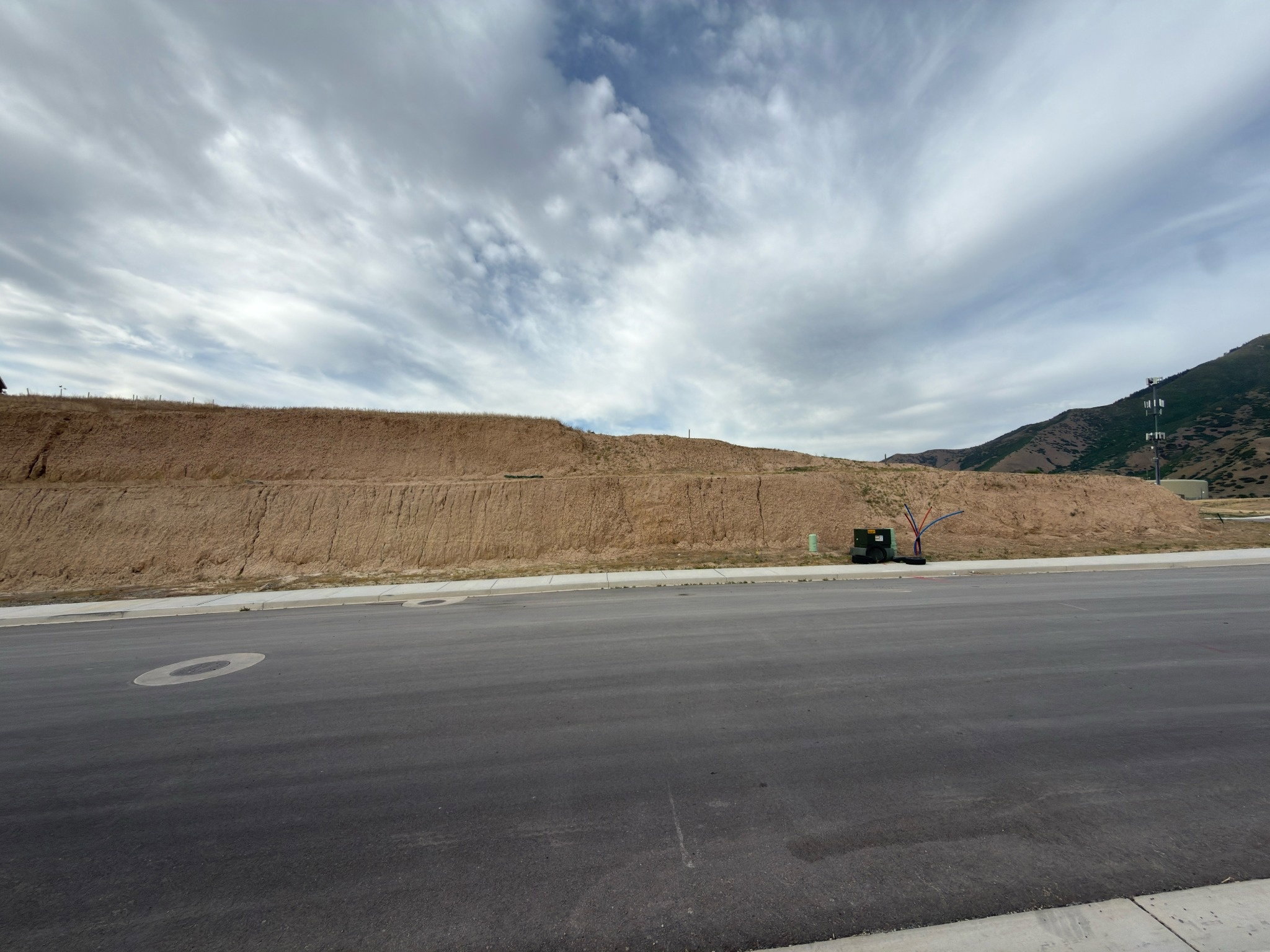 Street-level raw land parcel featuring an expansive graded dirt slope and a paved road