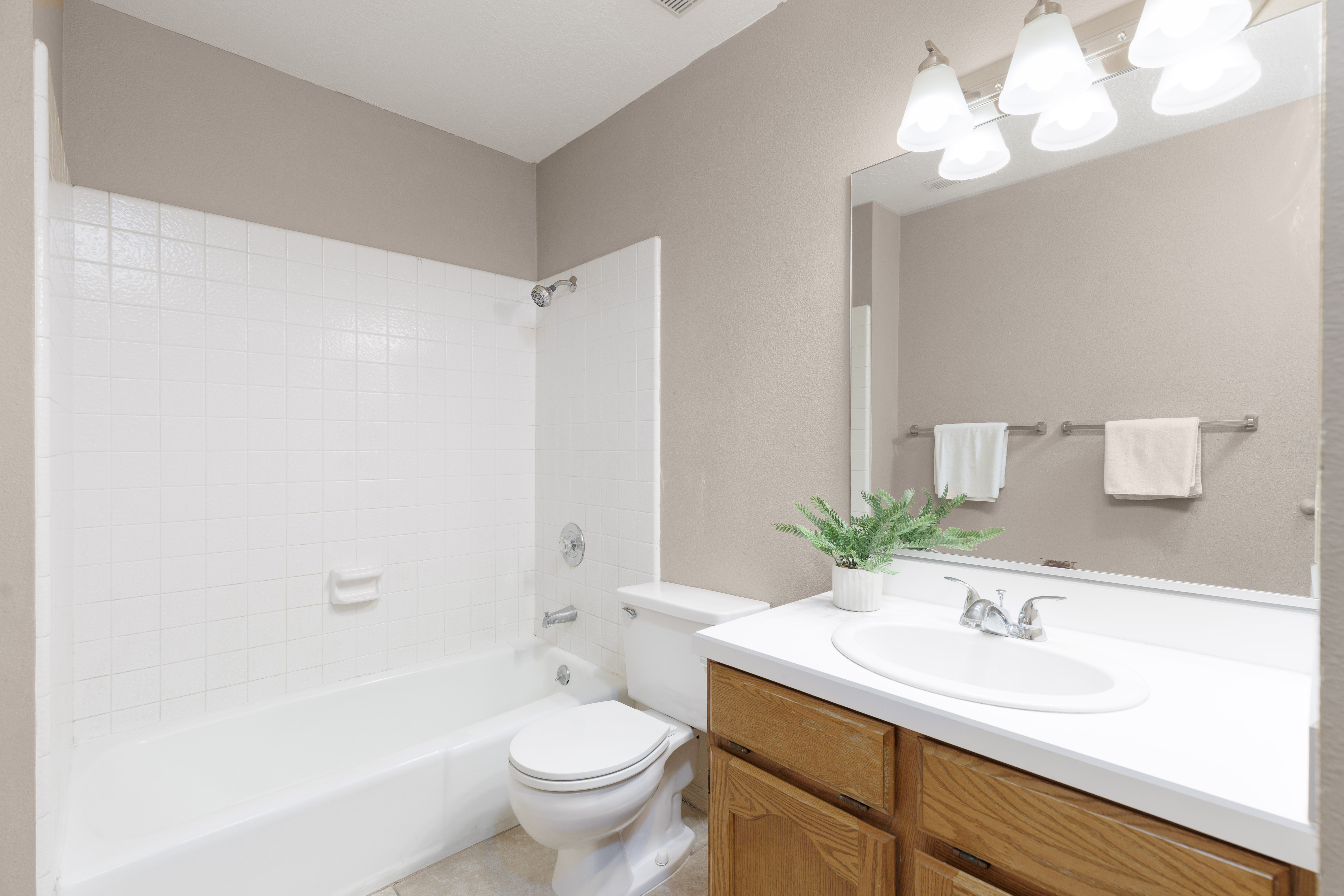 Owner Suite bathroom featuring a shower-tub combination with white subway tile surround, a single vanity with wood-finish cabinetry, a white countertop, and a large wall-mounted mirror