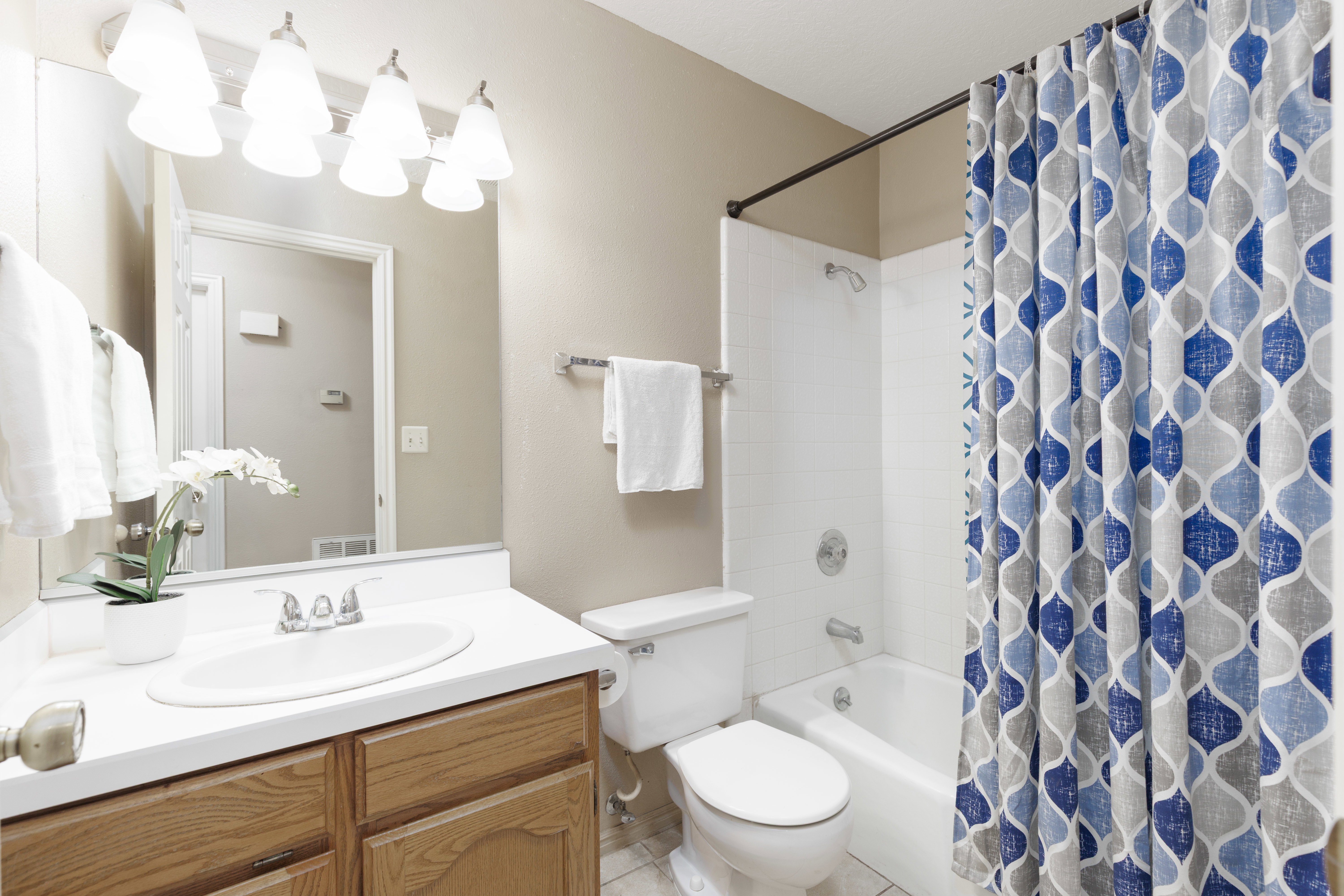 Bathroom featuring a built-in wood-finish vanity with a white countertop and integrated sink, a full vanity mirror, and a combined tub and shower with white subway tile surround