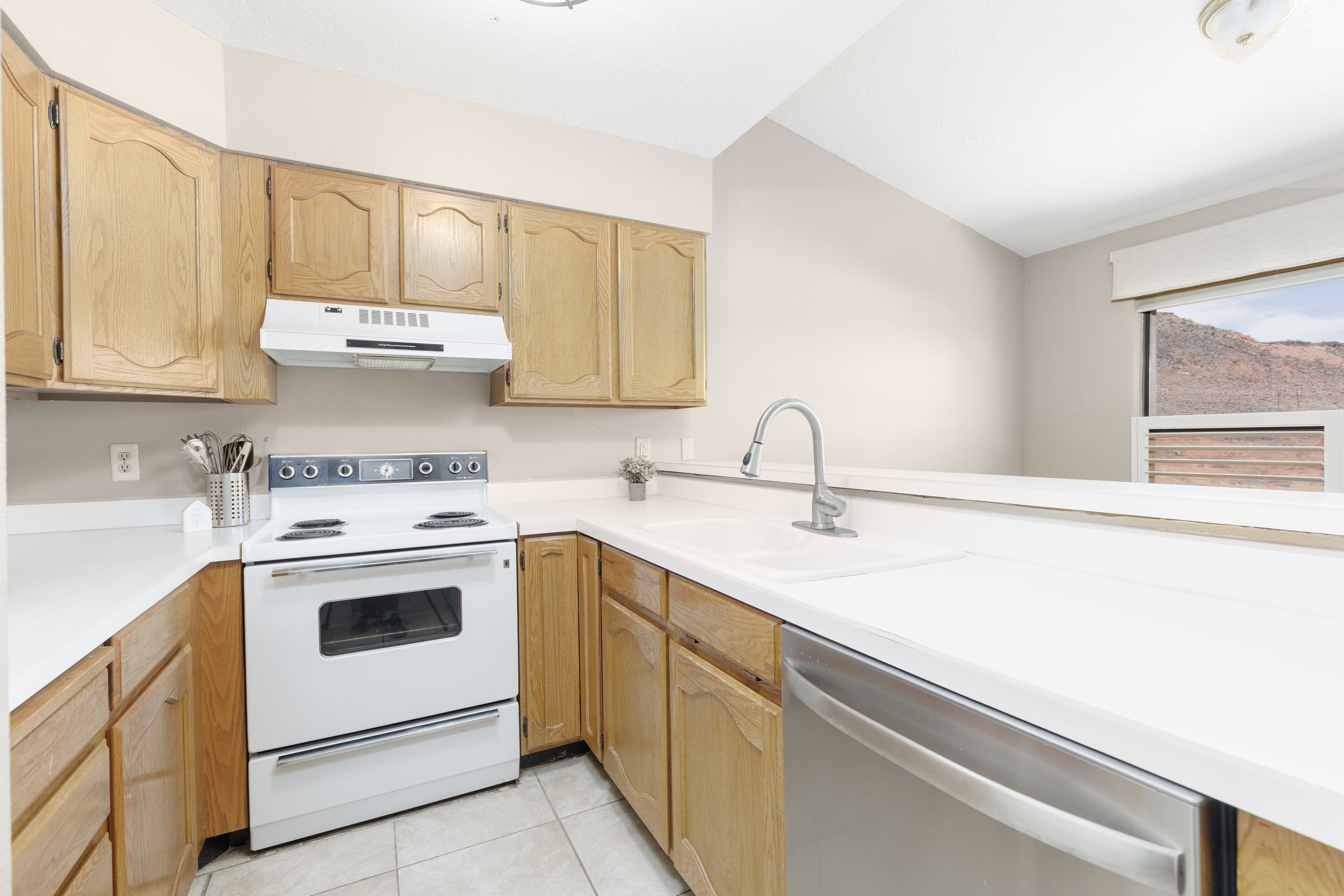 Kitchen featuring light wood cabinetry, white countertops, a white electric range, and a stainless steel dishwasher