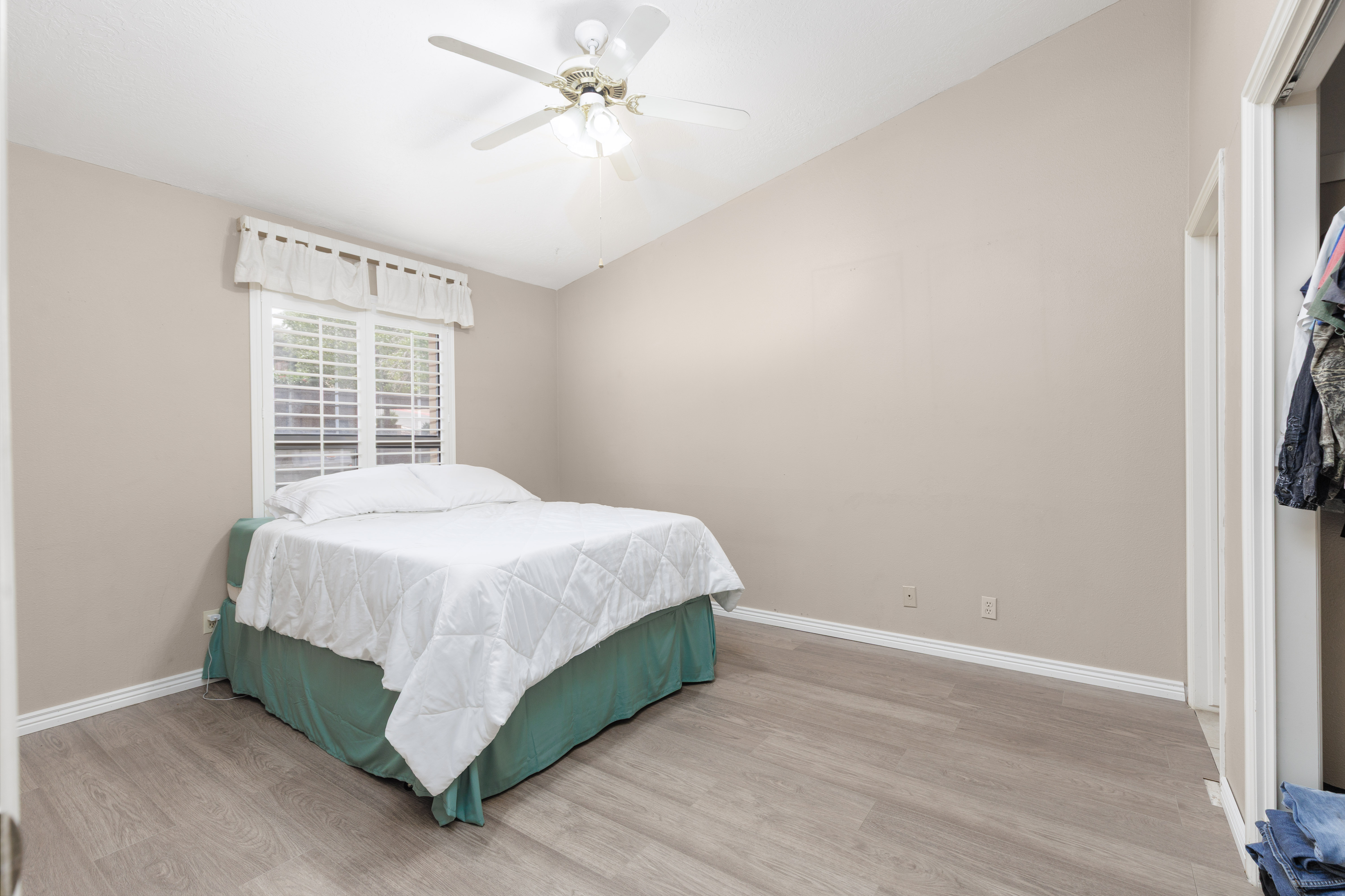 Interior room featuring vaulted ceilings, light wood-finish flooring, a window with white plantation shutters, and a ceiling fan with integrated lighting