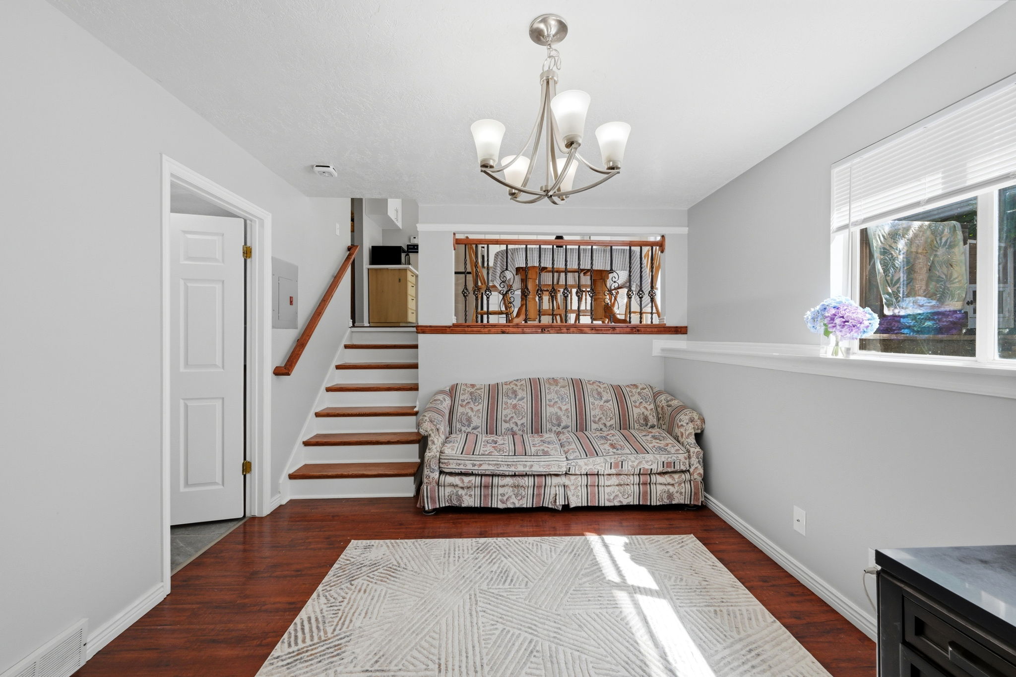 Spacious room featuring wood-finish flooring, a contemporary chandelier, and a large window with privacy blinds