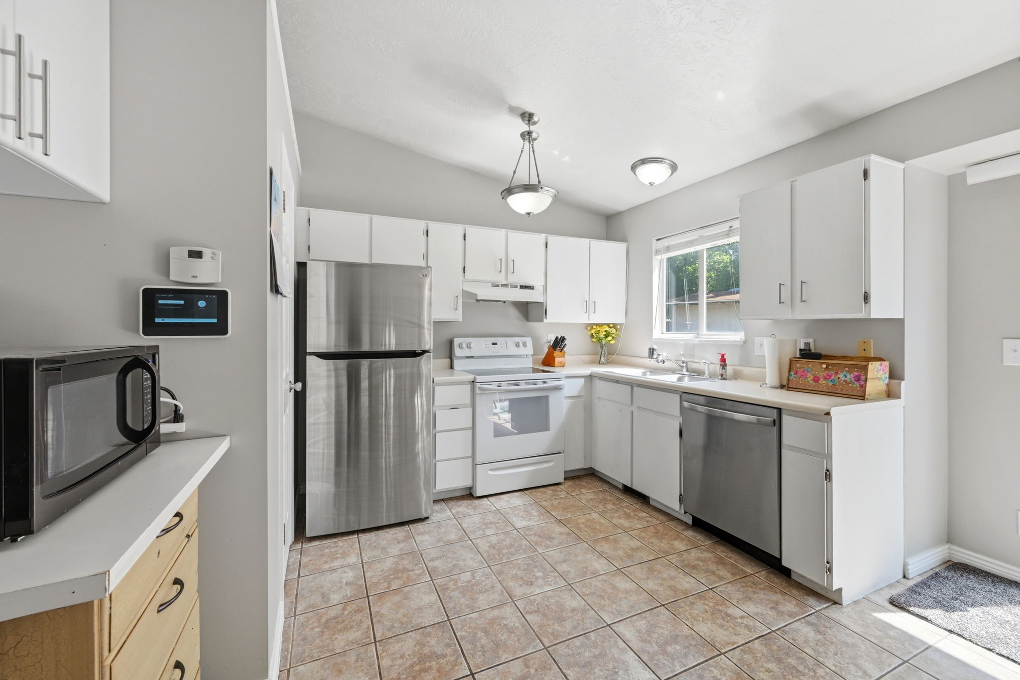 Kitchen featuring white cabinetry, stainless steel refrigerator and dishwasher, white range, and tiled flooring