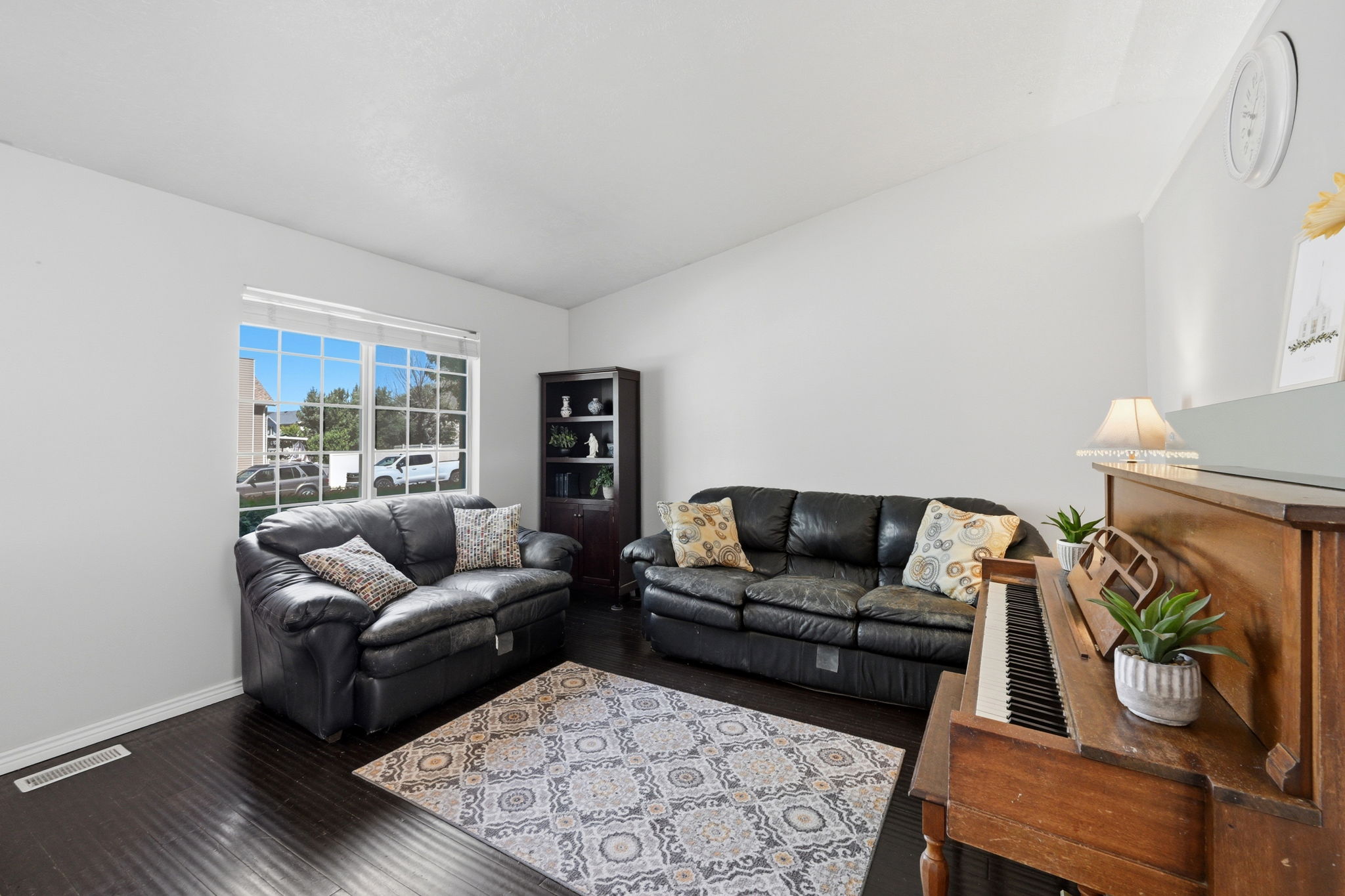 Spacious living area featuring dark wood-finish flooring, white wall tones, and a large multi-pane window