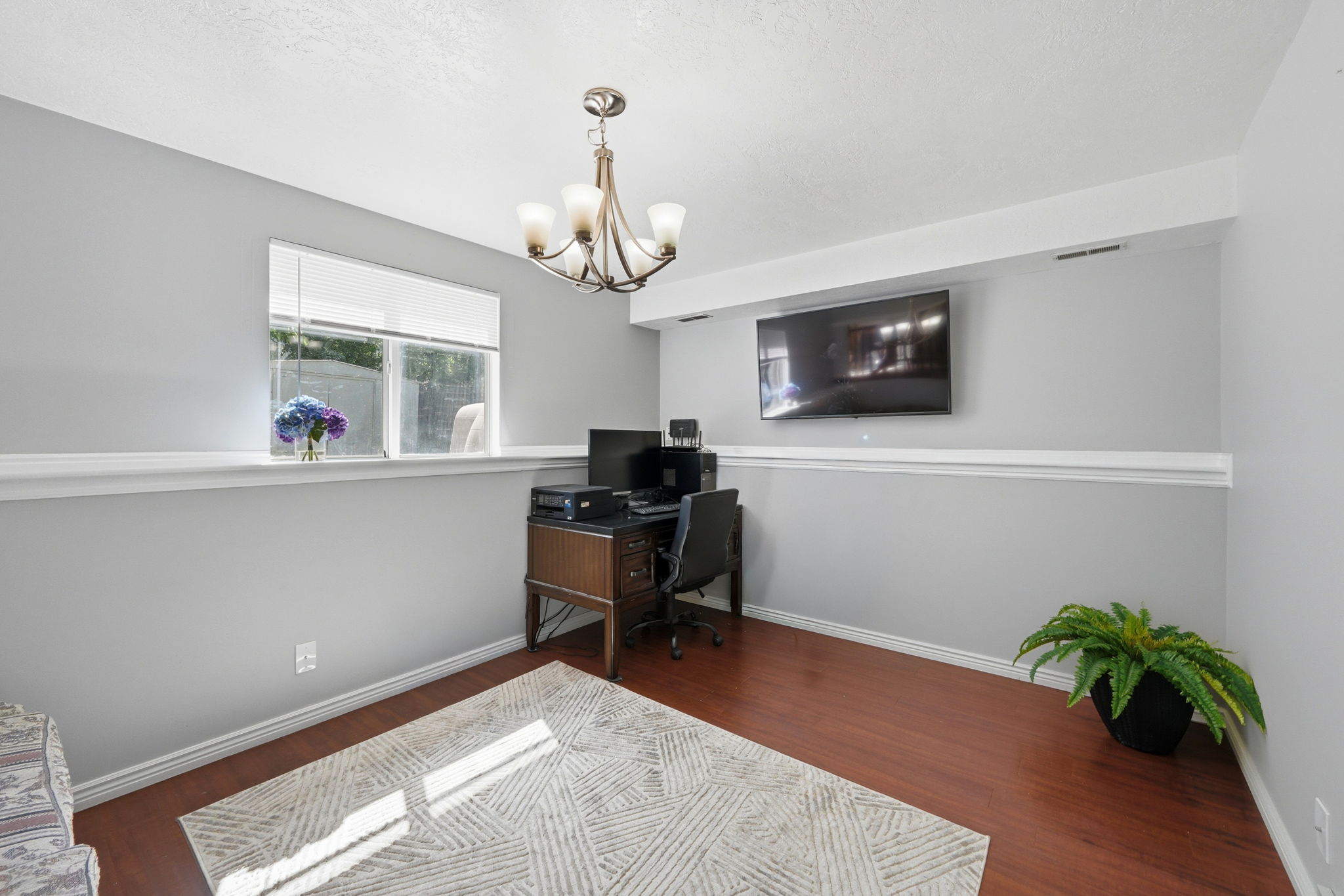 Room featuring wood-finish flooring, a wall-mounted display, and a decorative chandelier