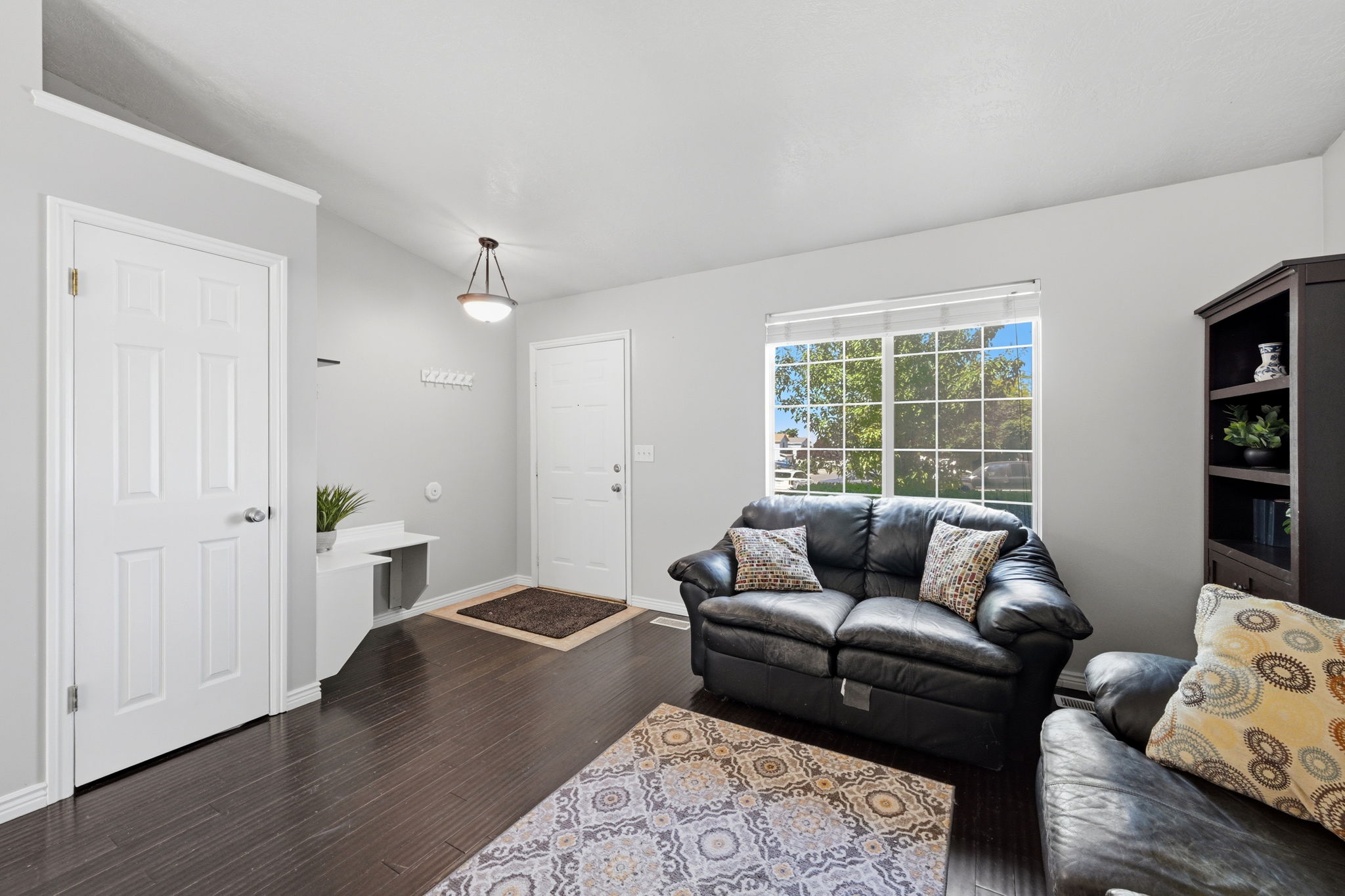 Spacious living area featuring dark wood-finish flooring, a large window with natural light, and light gray wall paint
