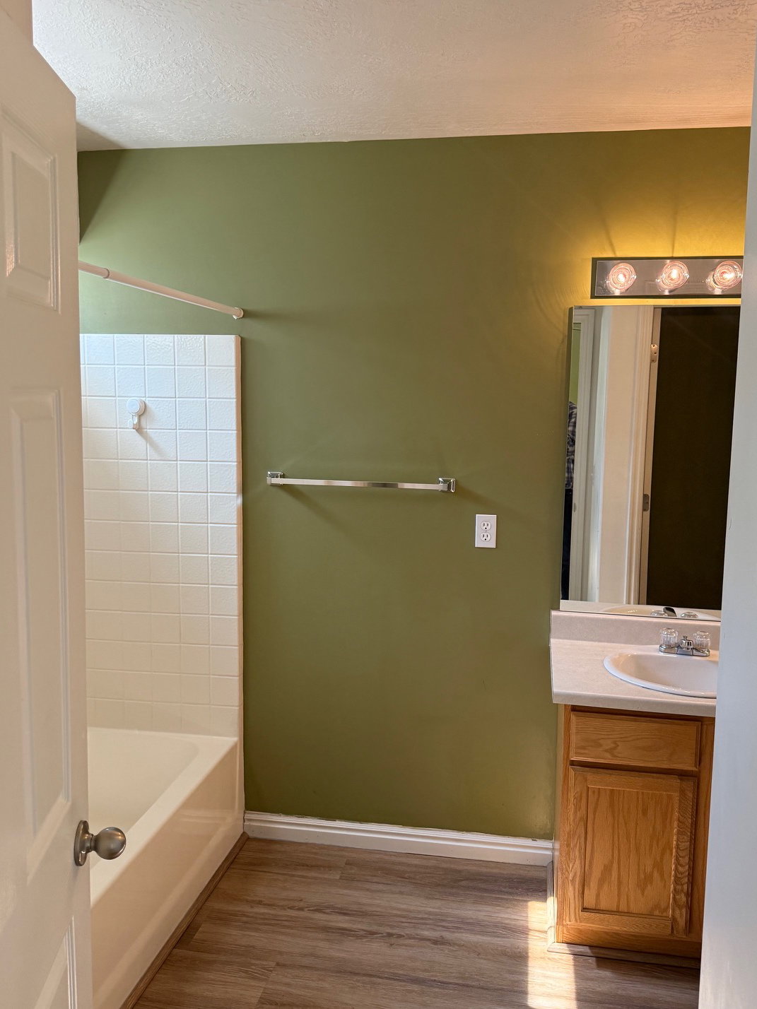Master Bathroom featuring a white tub with subway tile surround, wood-finish flooring, single vanity with light-toned countertop, and a wall-mounted mirror with an overhead light fixture
