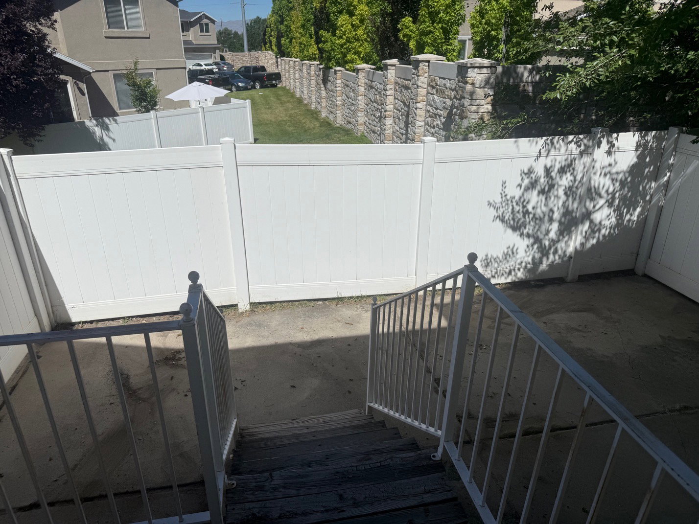 Rear concrete patio area featuring white vinyl fencing and a stone retaining wall