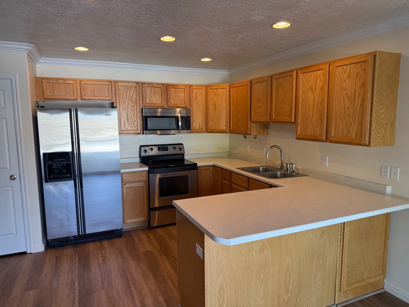 Kitchen featuring wood-finish flooring, stainless steel appliances, light wood cabinetry, and a double basin sink