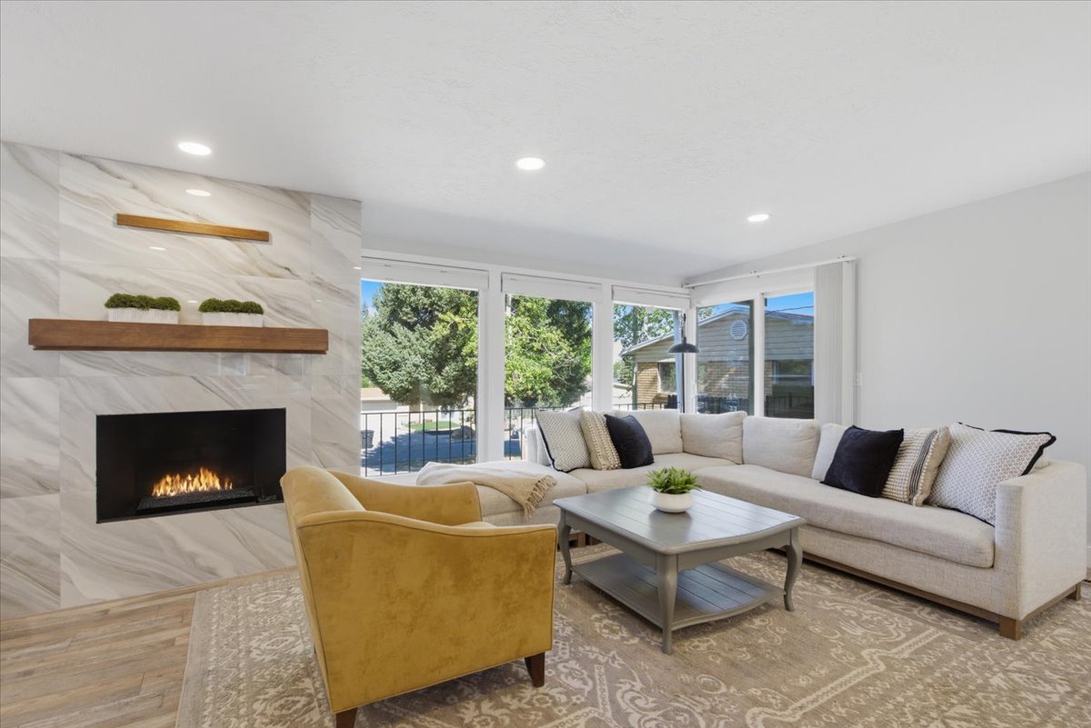 Living area featuring a tiled fireplace with wood mantels, wood-finish flooring, recessed lighting, and large windows