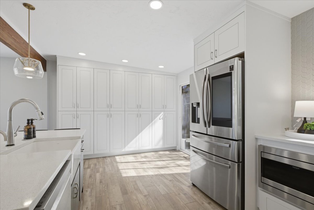 Modern kitchen featuring extensive white shaker cabinetry, stainless steel appliances, wood-finish flooring, recessed lighting, and a kitchen island with a built-in sink