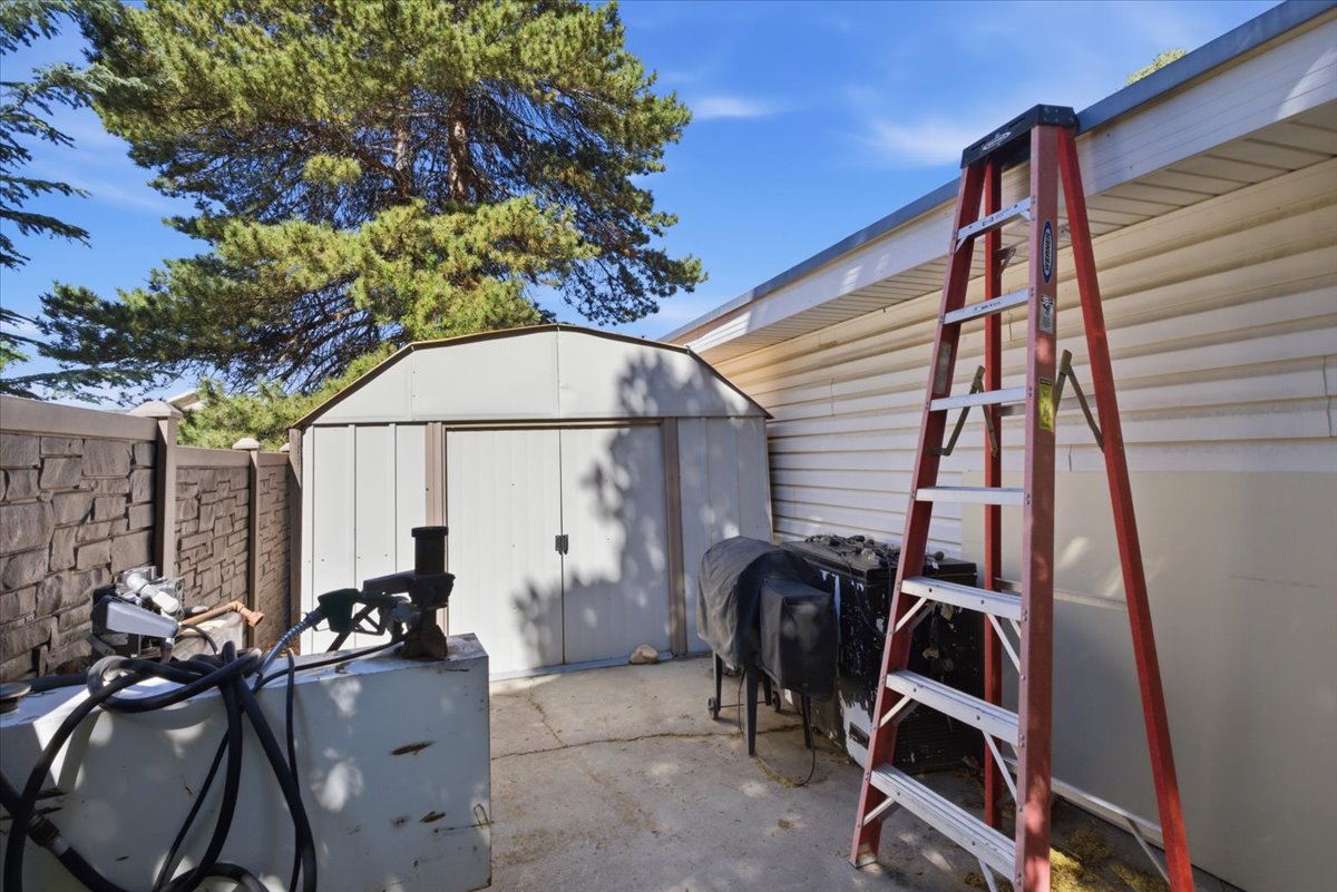 Exterior storage shed with a peaked roof, concrete patio, and a stone-look perimeter fence