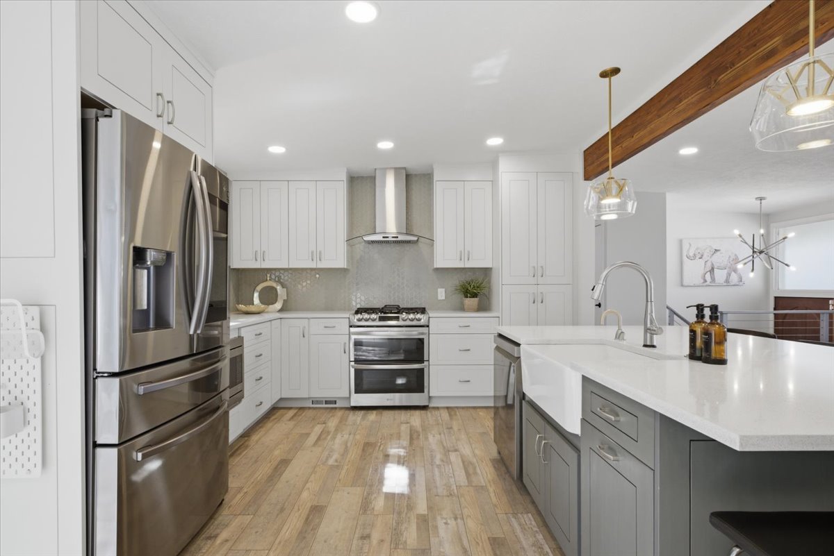 Modern kitchen featuring an expansive island with a farmhouse sink, stainless steel appliances, light wood-finish flooring, white cabinetry, and recessed lighting