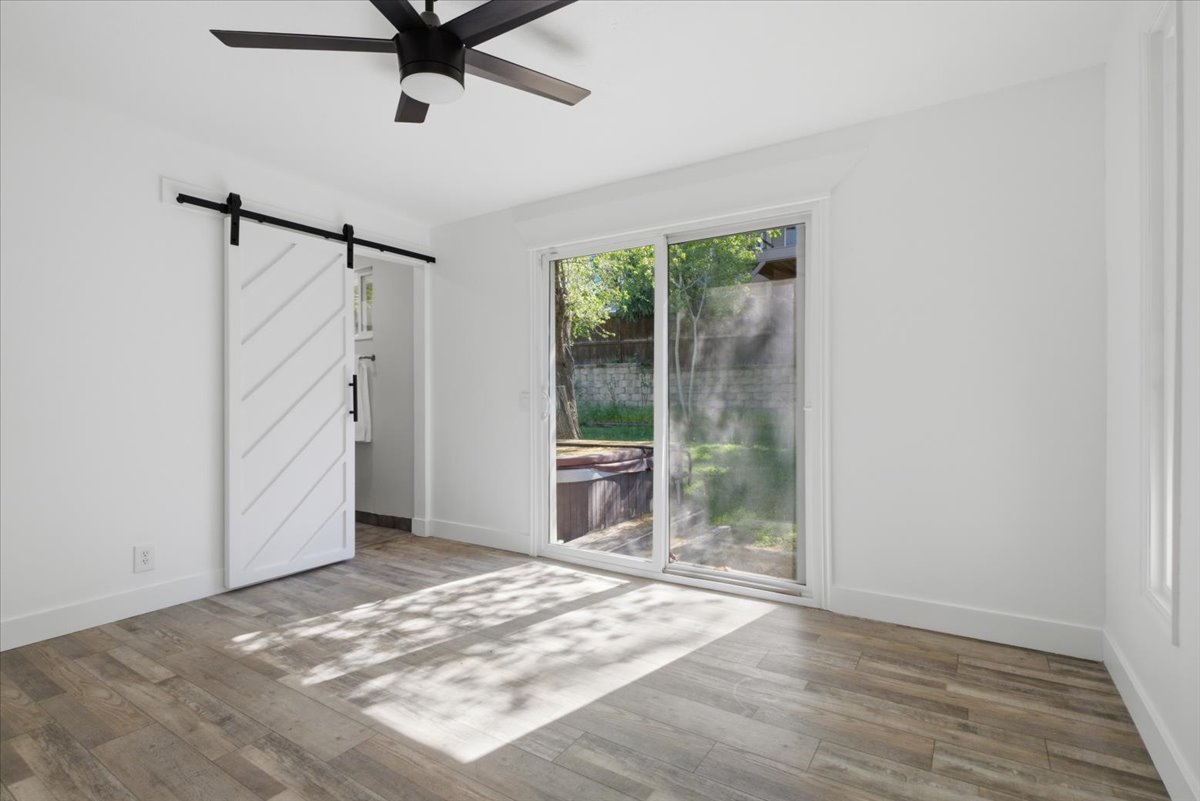 Spacious room featuring wood-finish flooring, a contemporary black ceiling fan, and a modern white barn door with black hardware