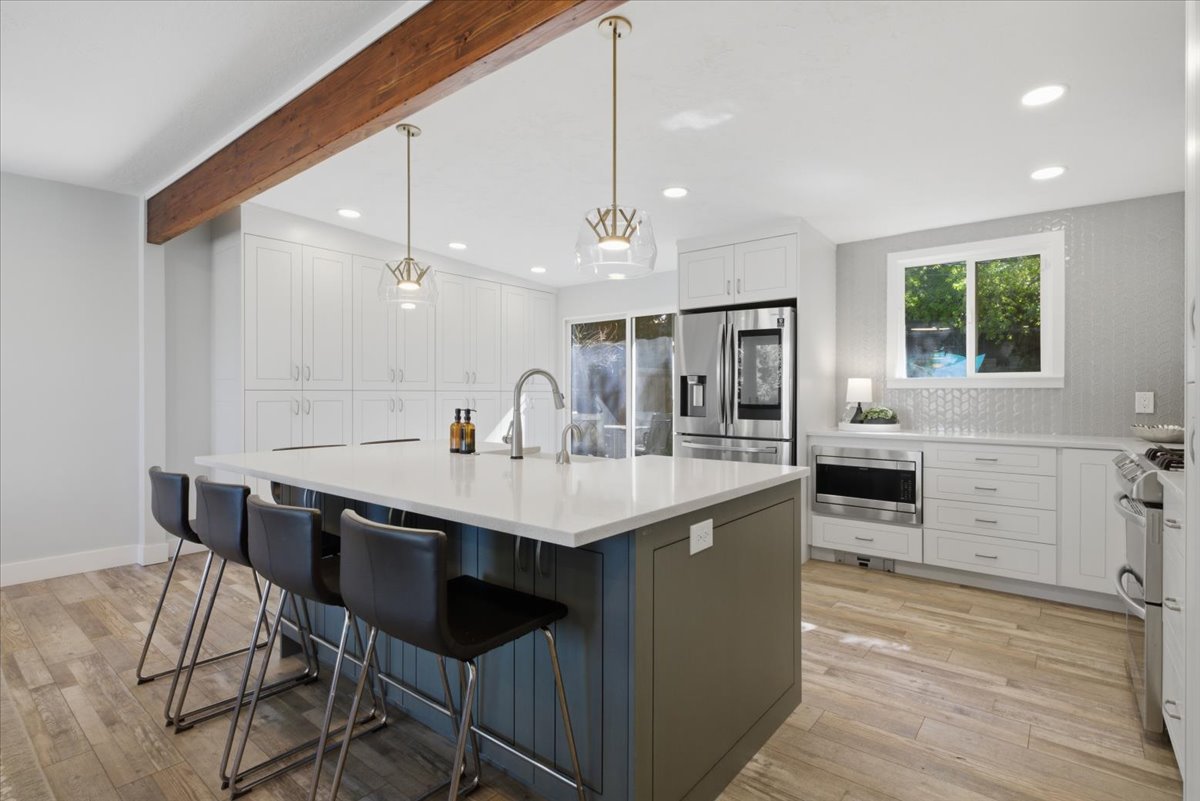 Modern kitchen featuring a large island with seating, pendant lighting, stainless steel appliances, extensive white cabinetry, and wood-finish flooring