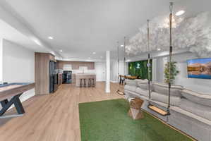Open-concept living area featuring wood-finish flooring, recessed lighting, and a modern kitchen with light wood cabinetry and dark appliances
