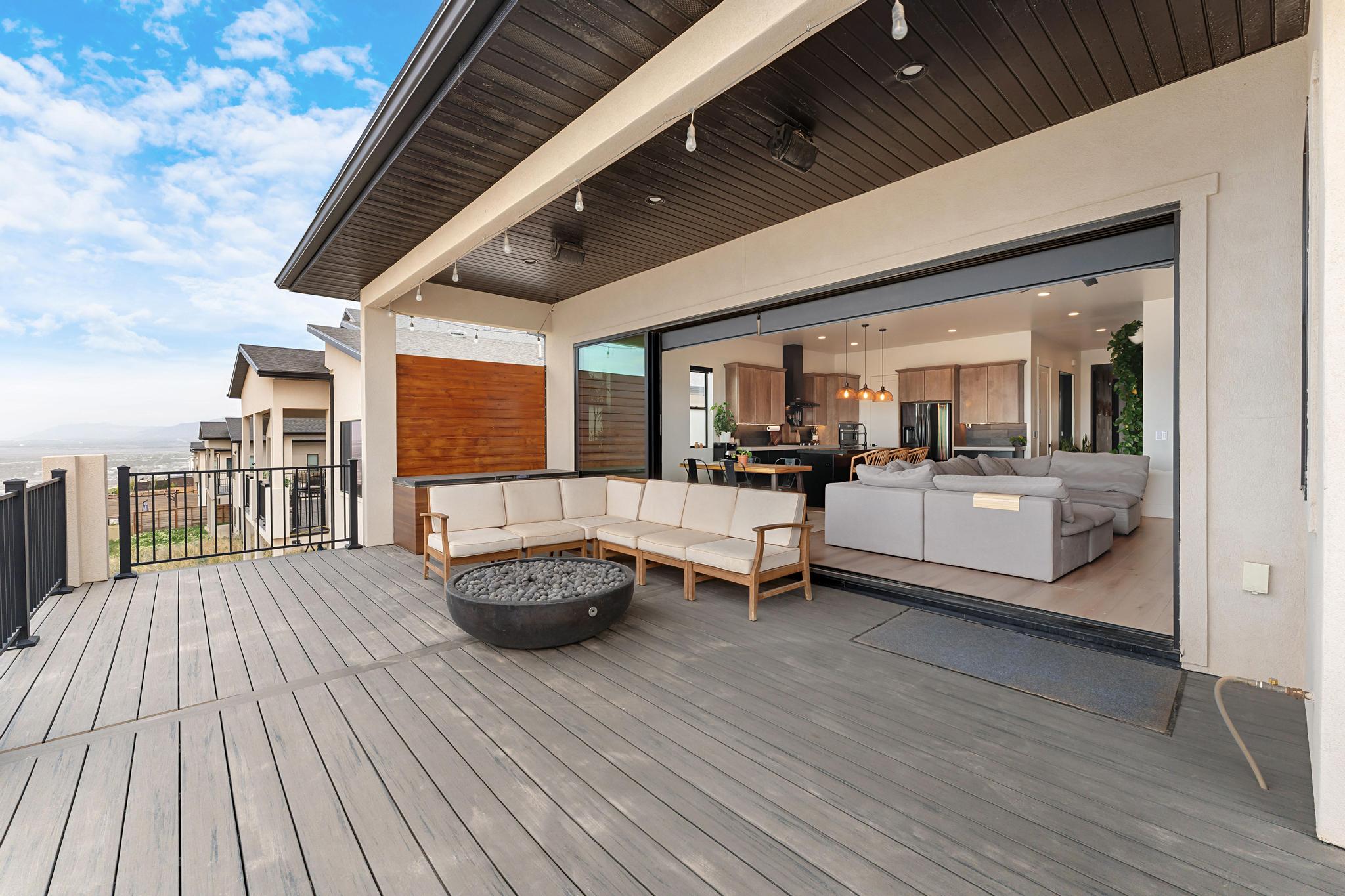 Expansive outdoor deck featuring wood-look composite decking, black metal railings, and a covered patio area with a dark wood-paneled ceiling