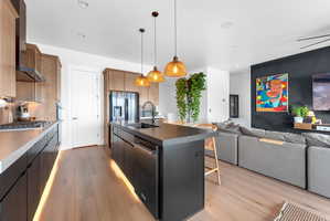 Open-concept kitchen and living area featuring wood-finish flooring, recessed lighting, and a dark accent wall