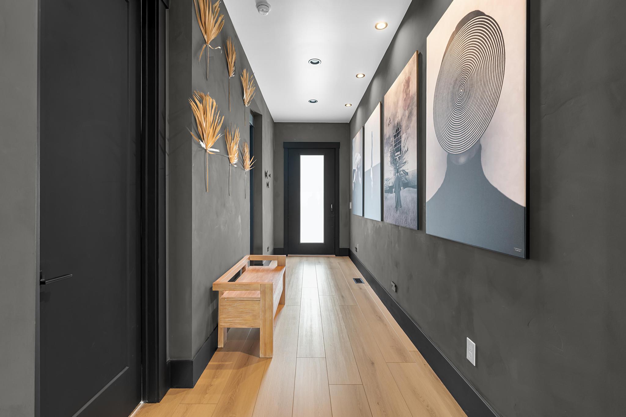 Hallway featuring light wood-finish flooring, dark textured walls, recessed ceiling lighting, and a full-light panel door