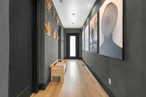 Hallway featuring light wood-finish flooring, dark textured walls, recessed ceiling lighting, and a full-light panel door