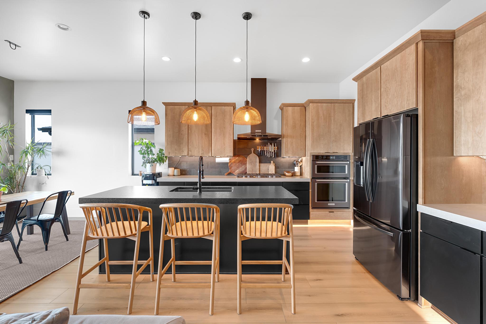 Modern kitchen with light wood-finish flooring and a large island featuring a black countertop and integrated sink