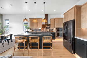 Modern kitchen with light wood-finish flooring and a large island featuring a black countertop and integrated sink